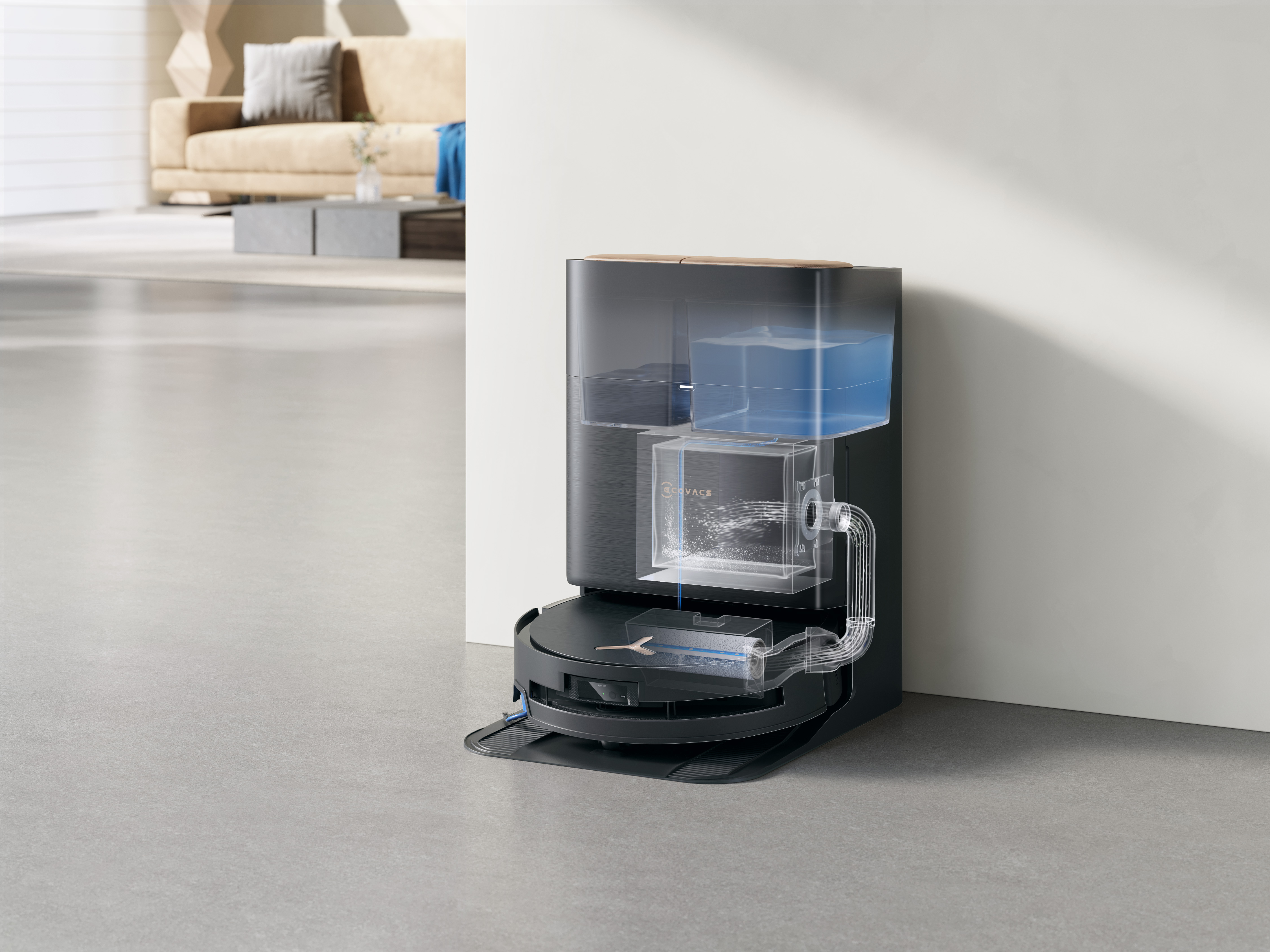 Robot sprzątający z pojemnikami na wodę, pokazujący wewnętrzne komponenty. Beżowa sofa i szara podłoga w tle.