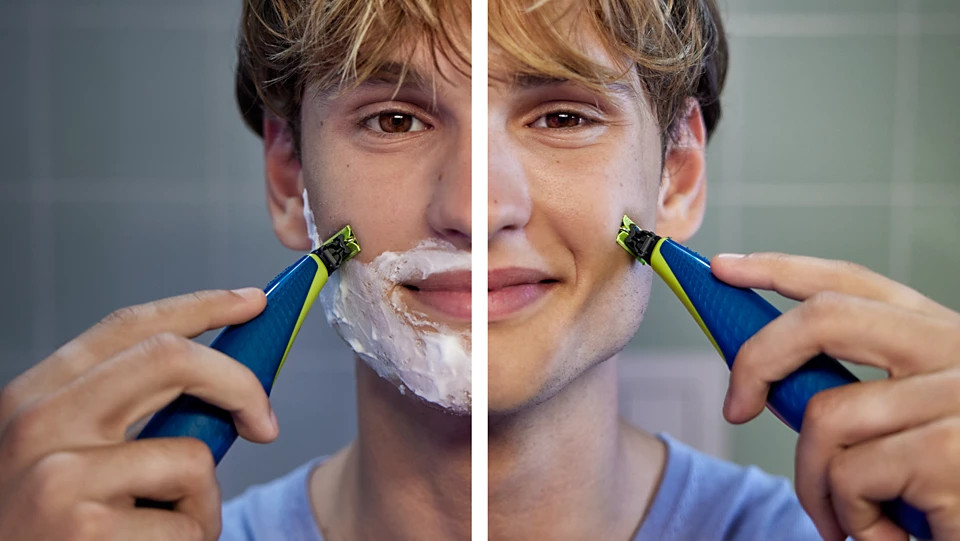 Mężczyzna goli się niebiesko-żółtą trymerem. Jedna strona jego twarzy ma krem do golenia, druga jest czysta i uśmiechnięta.