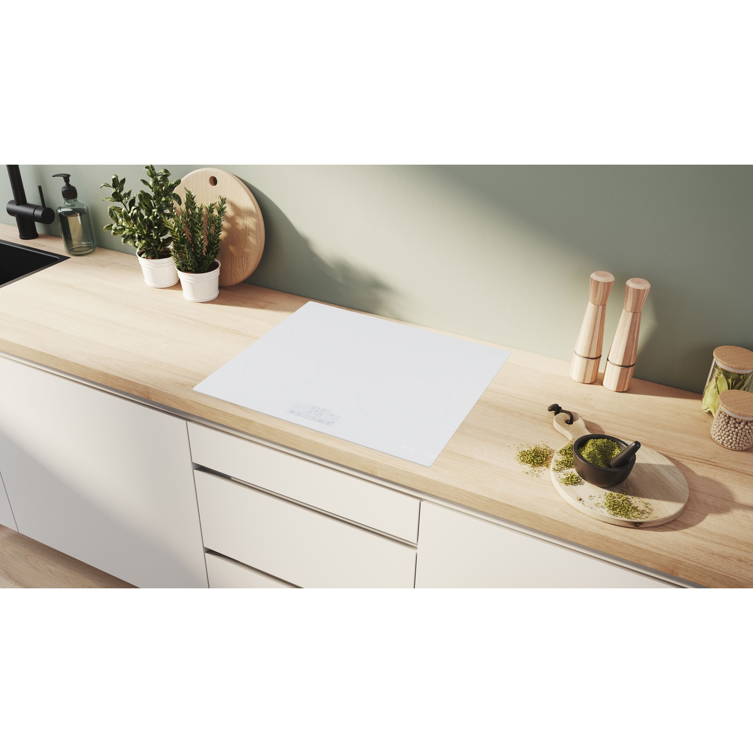 Piano cucina con piano cottura bianco. Erbe, spezie, piante e assi di legno sono disposte. Sfondo: parete verde chiaro e armadi bianchi.