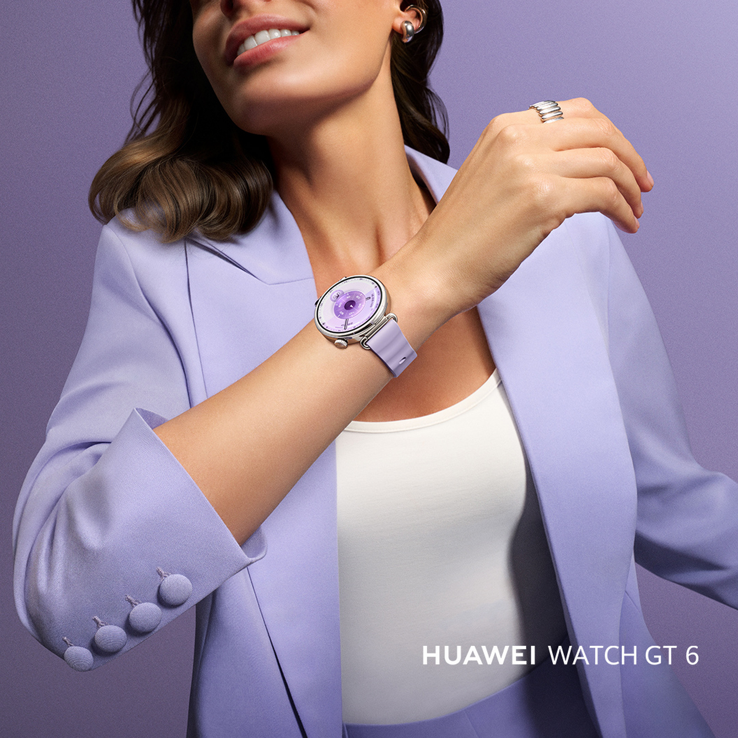 Mujer con un smartwatch, en un traje morado, sonriendo. El reloj está en su muñeca. El fondo es morado.
