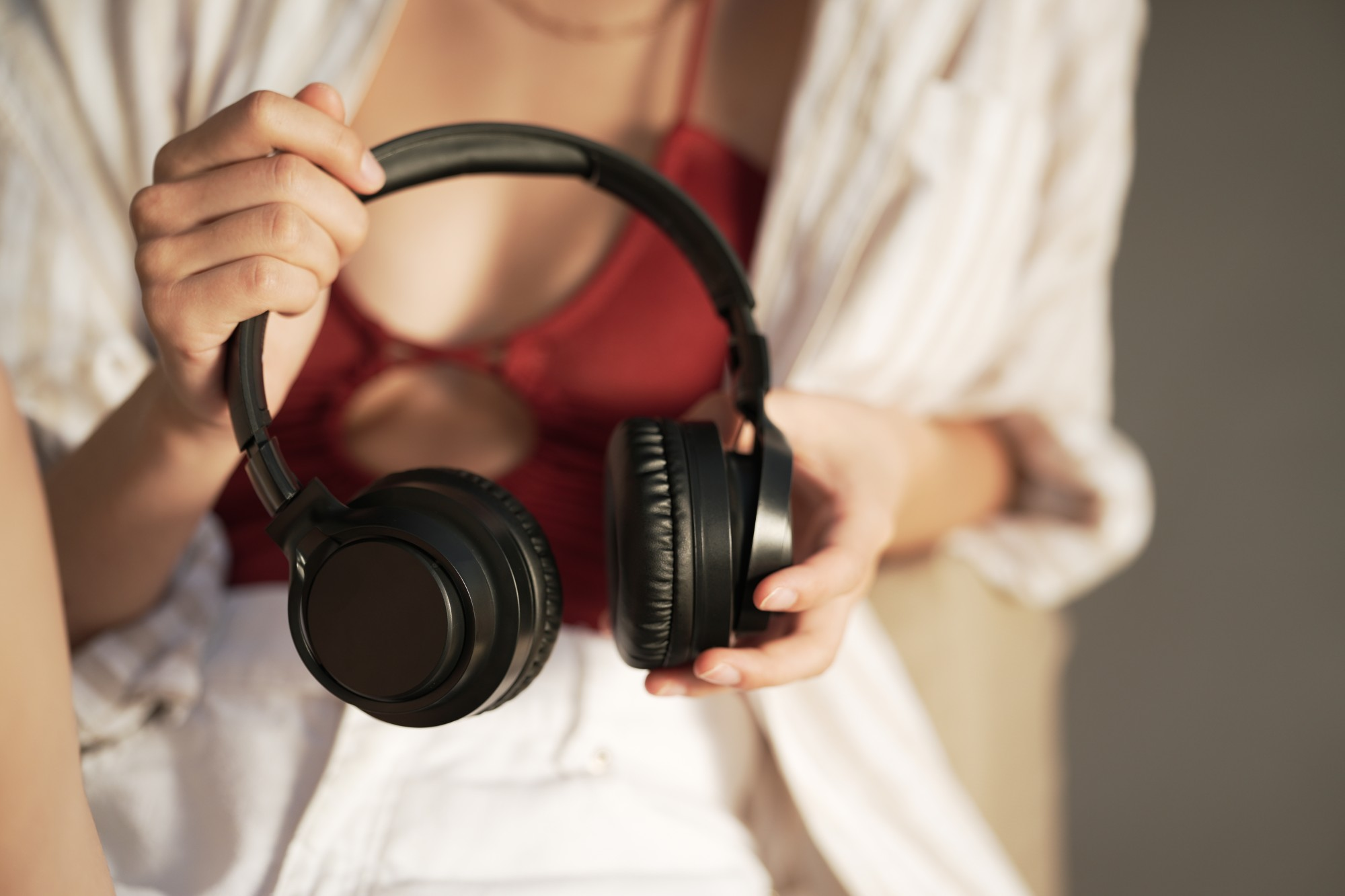 Osoba trzyma czarne słuchawki. Ma na sobie czerwoną bluzkę pod białą koszulą.