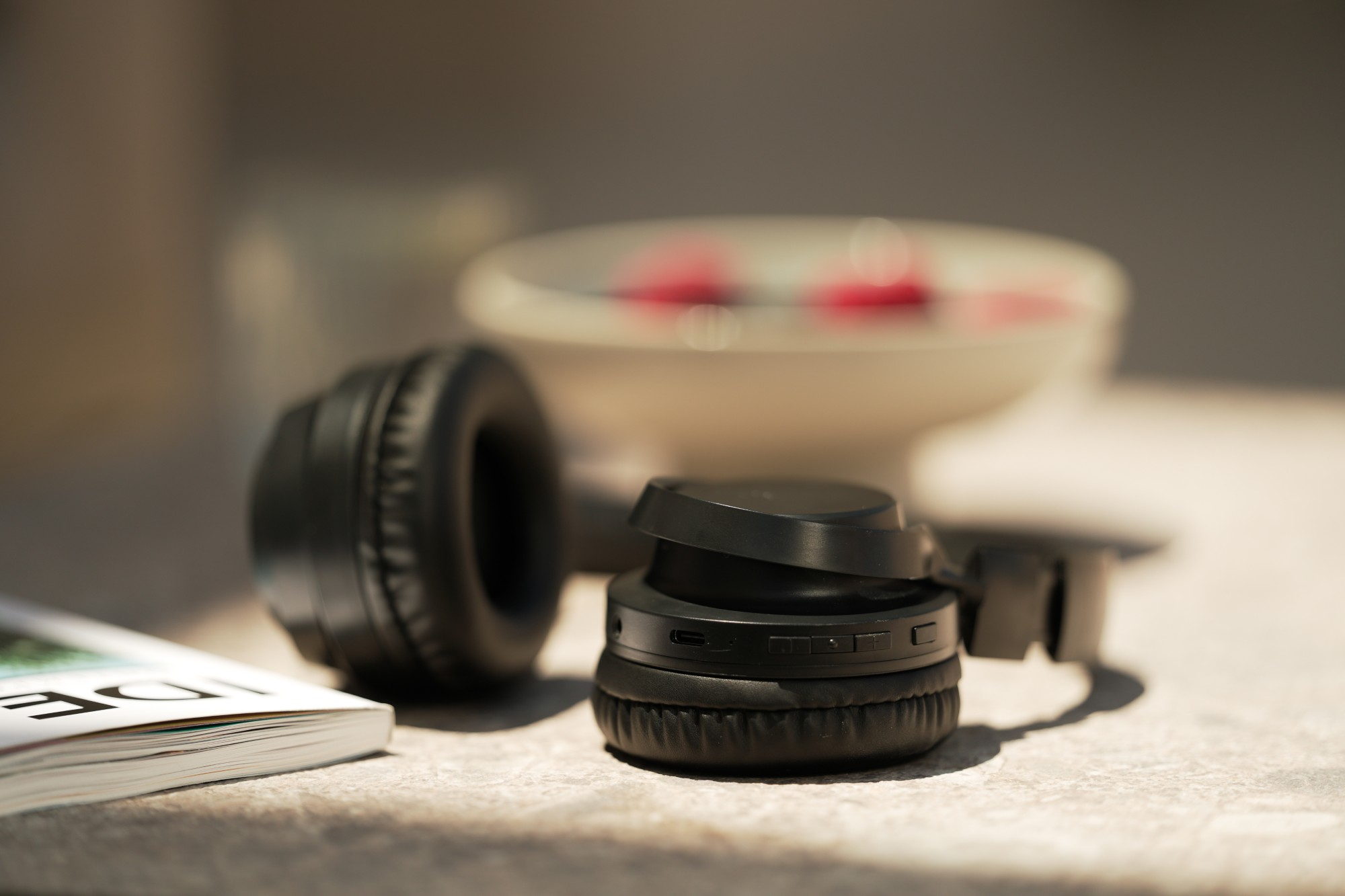 Czarne słuchawki na powierzchni z książką i miską z czerwonymi elementami w tle.