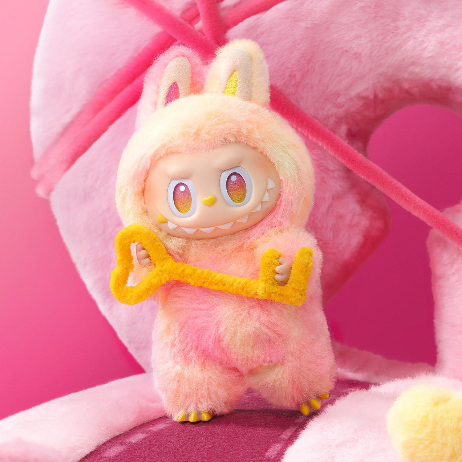 Una figura di coniglio rosa di peluche tiene in mano una chiave gialla. Lo sfondo ha la forma di una ciambella rosa.