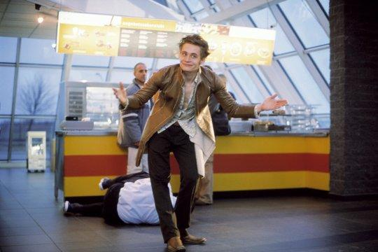 Mann mit ausgestreckten Armen vor einem Imbissstand, eine andere Person liegt am Boden, und zwei weitere stehen.