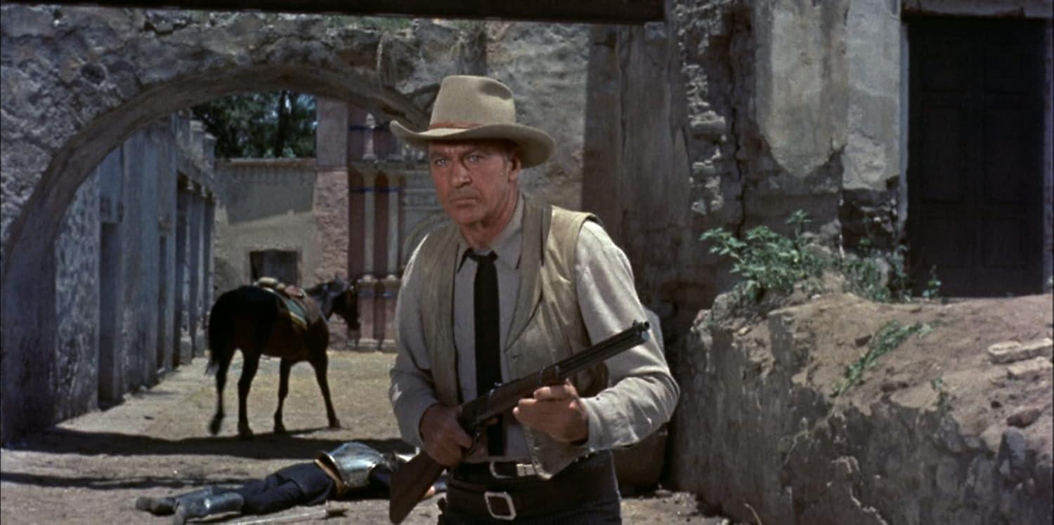 Ein Mann mit Cowboyhut und Weste hält ein Gewehr. Ein Pferd steht hinter ihm, und eine Person liegt am Boden.
