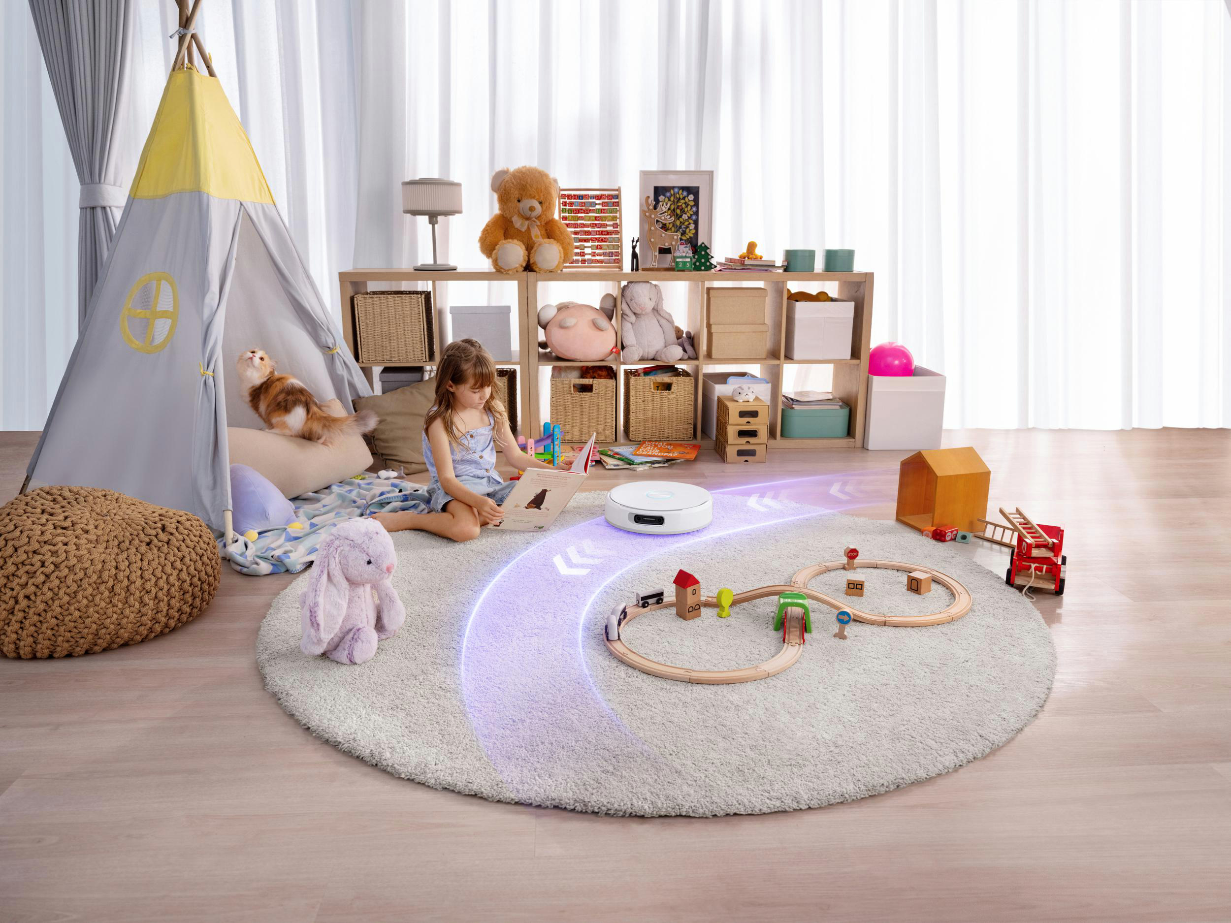 Ein Mädchen liest auf einem Teppich. Ein Roboterstaubsauger reinigt. Spielzeug und ein Tipi sind im Hintergrund.