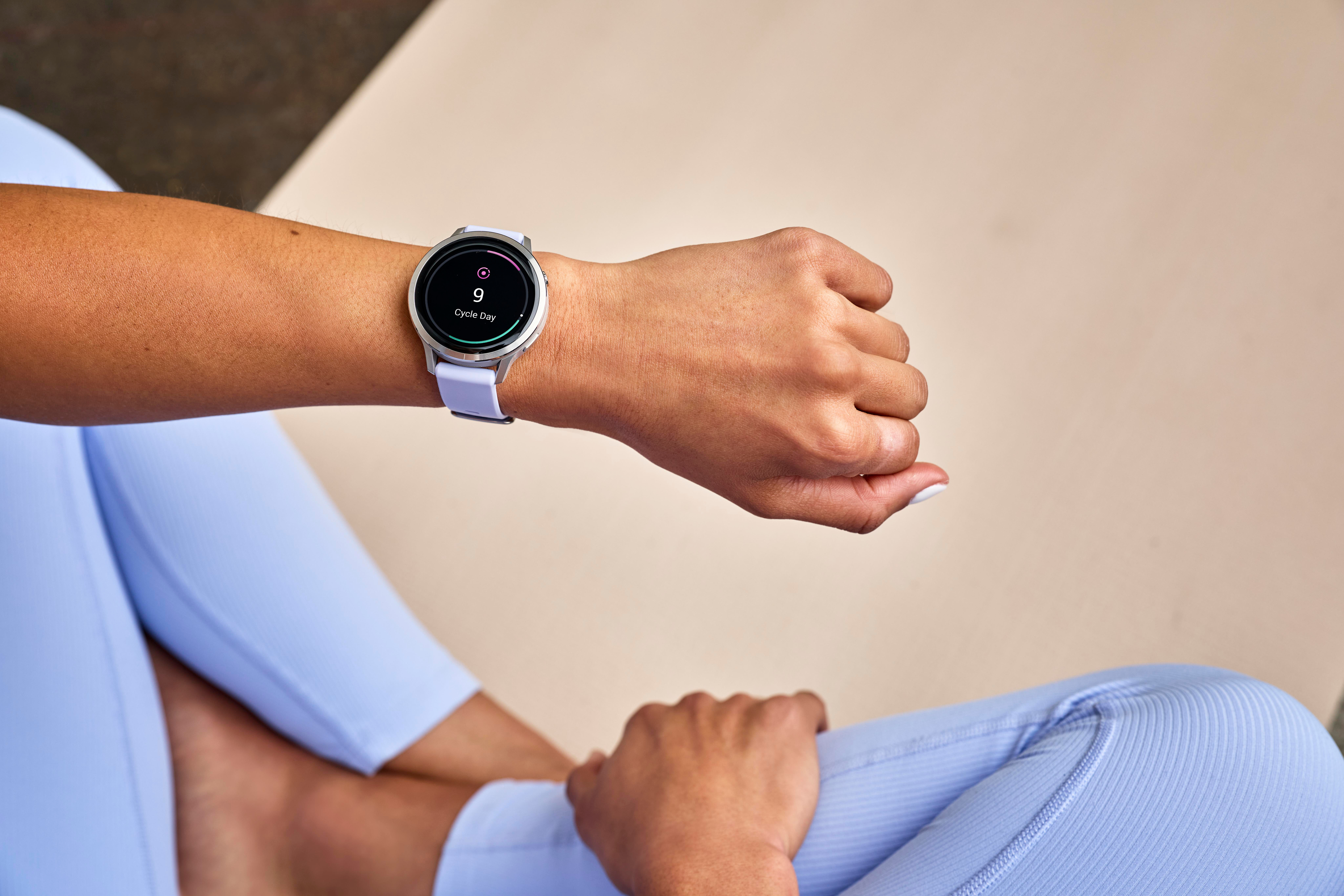 Eine Person mit Smartwatch, die den 9. Zyklustag anzeigt. Die Person trägt hellblaue Leggings und sitzt auf einer Matte.