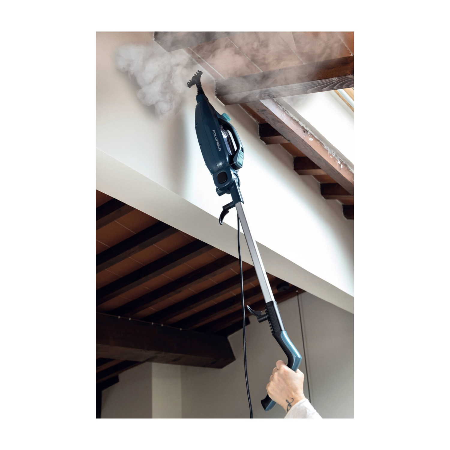 Una persona usa un pulitore a vapore su un soffitto con travi in legno. Il vapore è visibile. Il pulitore è verde acqua e argento.