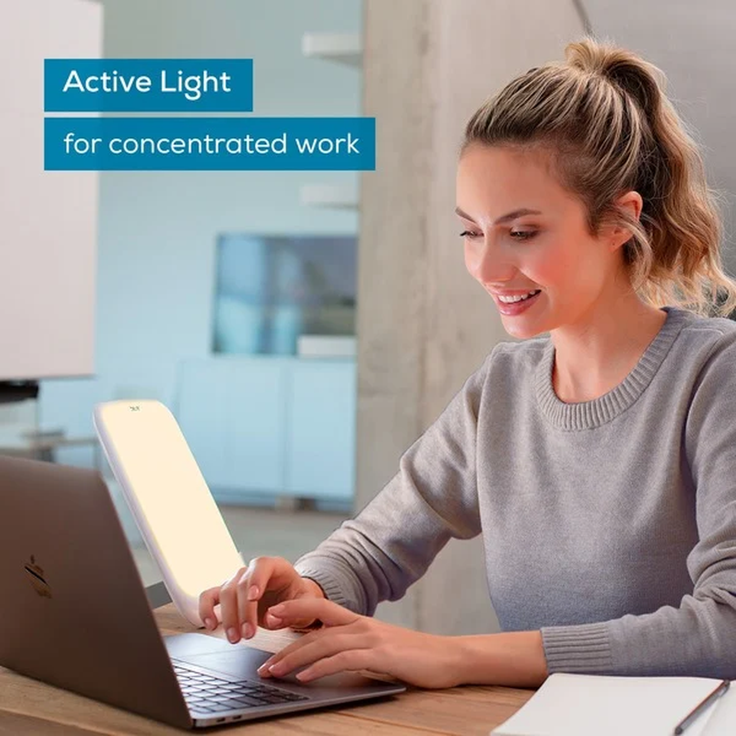 A woman smiles while working on a laptop with an active light on a wooden desk. Text reads 'Active Light for concentrated work'.