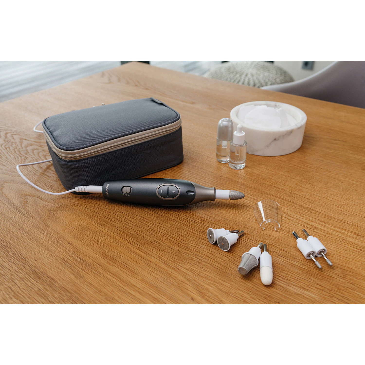 Nail care kit on a wooden table. Includes a grey case, nail file, accessories, and a bowl with a cotton pad.