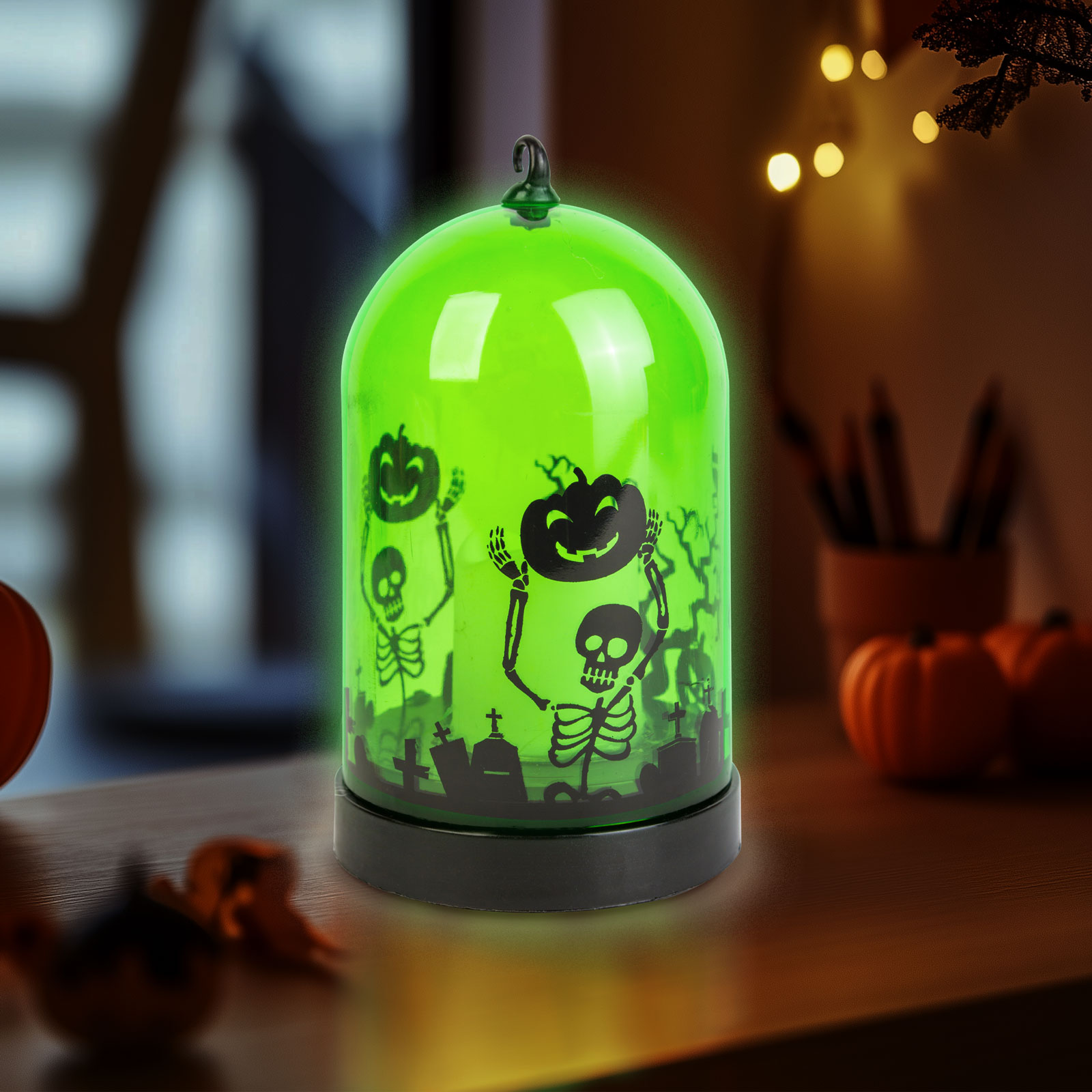 Zöld Halloween dekoráció csontvázakkal és tökökkel egy üvegkupolában, fa felületen, tökökkel a háttérben.