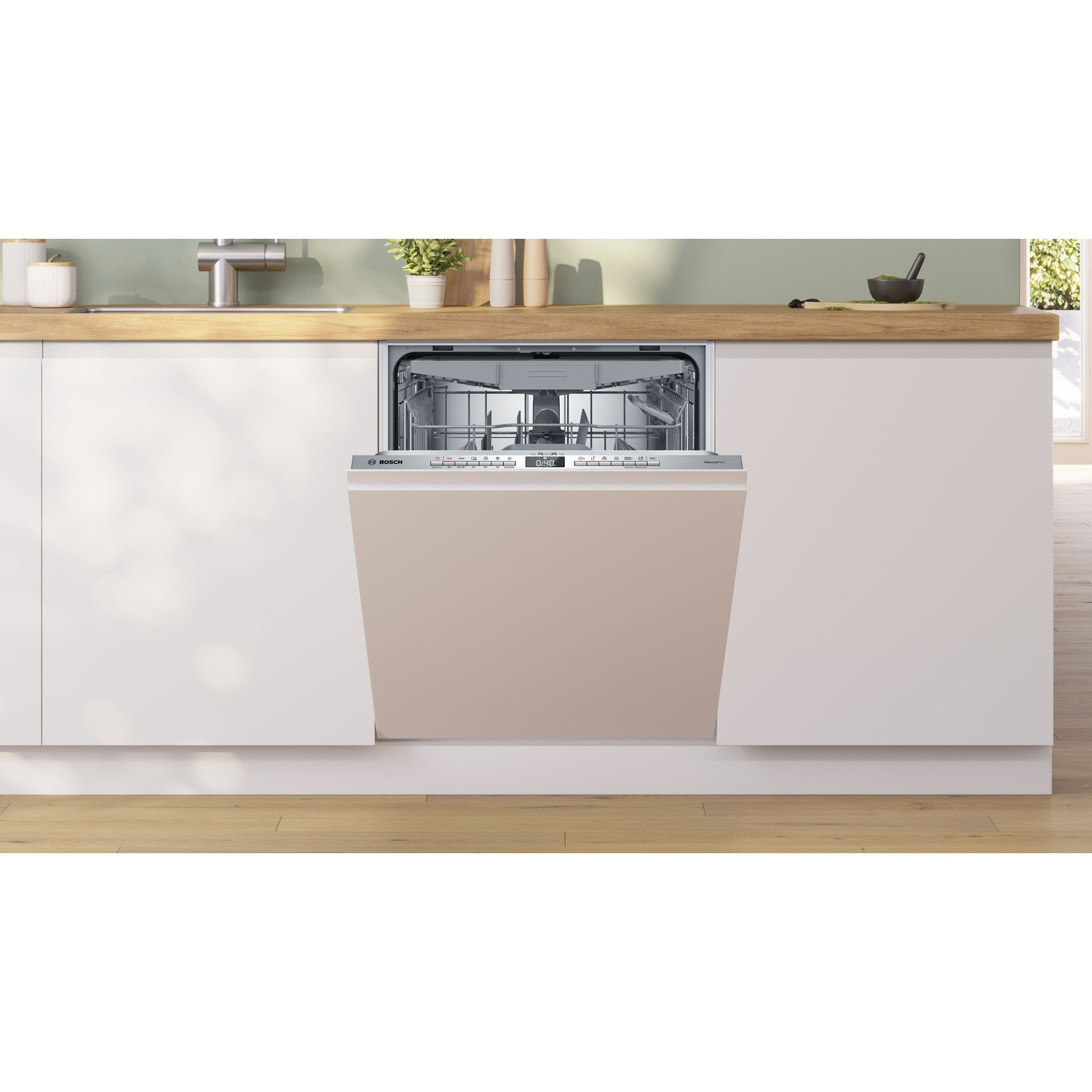 Una lavastoviglie aperta con porta beige, integrata in mobili bianchi, in una cucina. Lo sfondo mostra un piano di lavoro con piante.