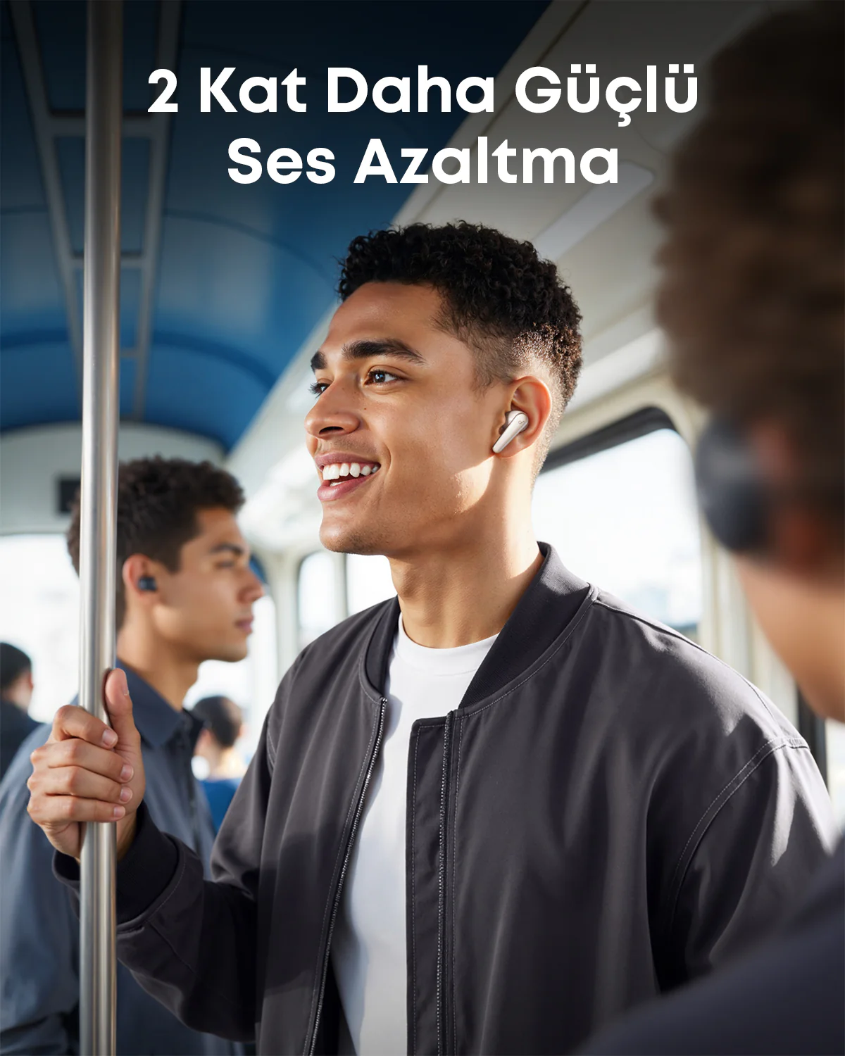 Trende kulaklık takan, gülen bir adam. Bir direğe tutunuyor. Arka planda başka insanlar var.