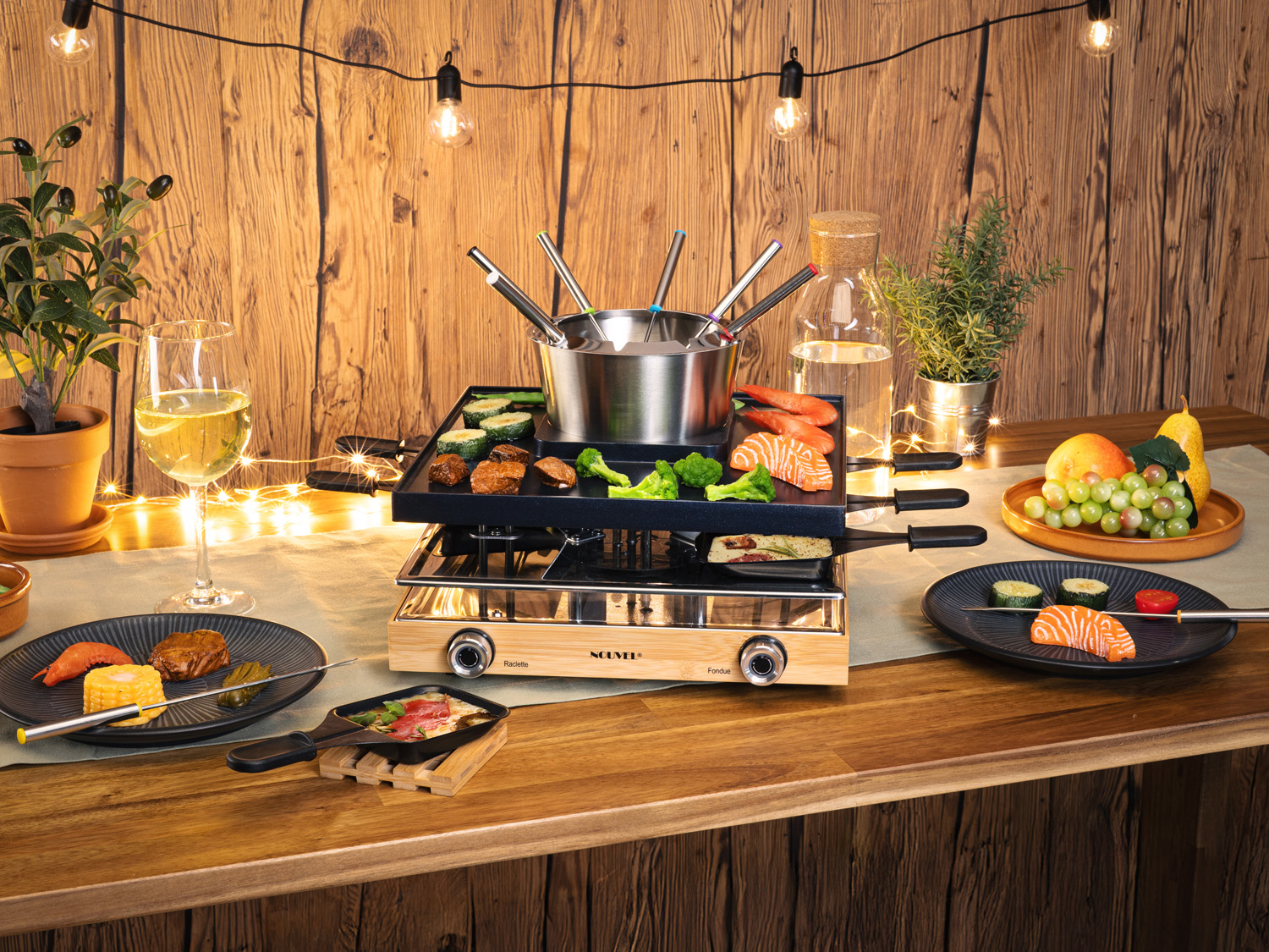 Una scena da tavolo con griglia per raclette, vari cibi, calice di vino e luci decorative davanti a uno sfondo di legno.