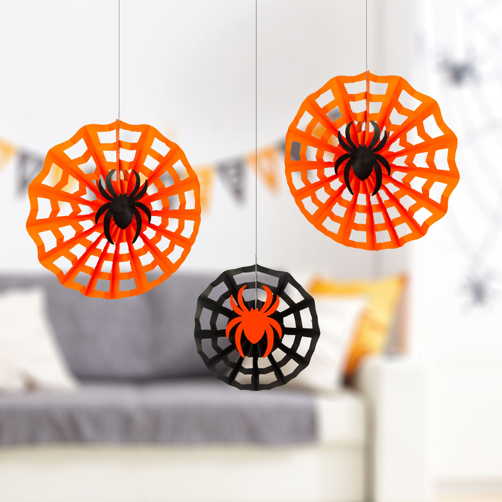 Három Halloween dekoráció: narancssárga és fekete pókhálók pókokkal, elmosódott háttérrel.