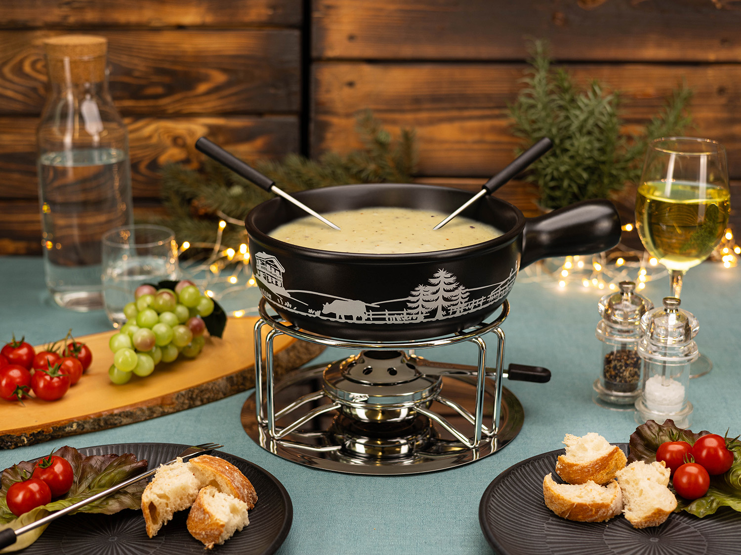 Un caquelon à fondue avec un brûleur allumé, du pain, des tomates, des raisins et un verre de vin sont sur une table avec un fond en bois.