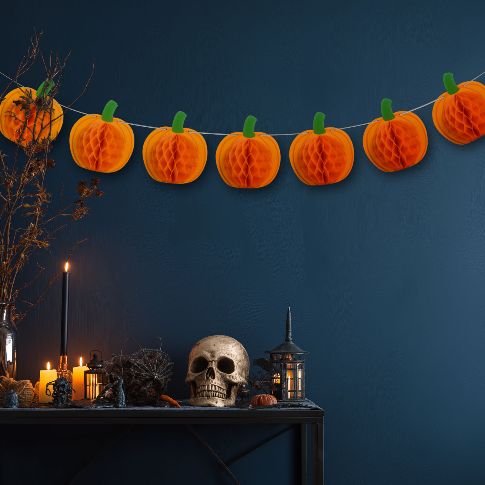 Halloween dekorációk: tökfüzér, koponya, gyertyák és lámpás sötétkék háttér előtt.