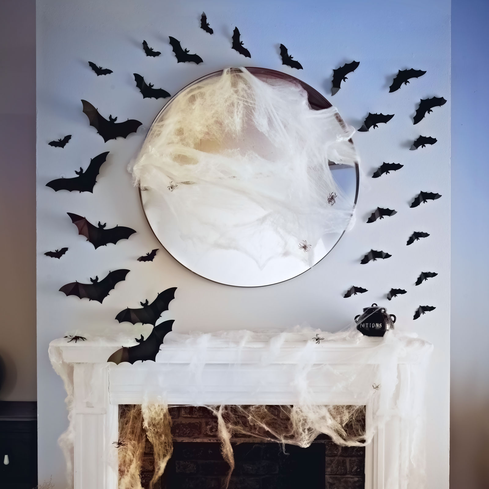 Egy Halloween-jelenet: denevérek, pókok és pókhálók díszítenek egy tükröt és egy kandallót. Egy üst a kandallópárkányon.