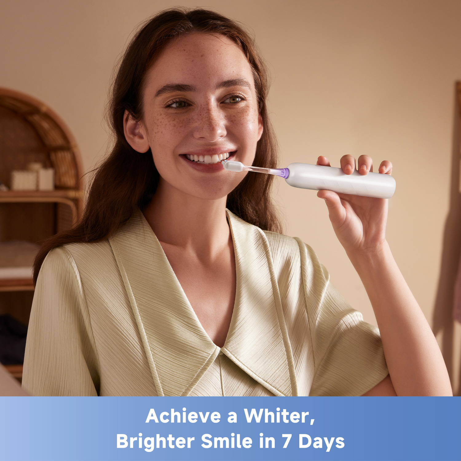 A woman smiles while using an electric toothbrush. The background shows a neutral-toned room with a decorative object.