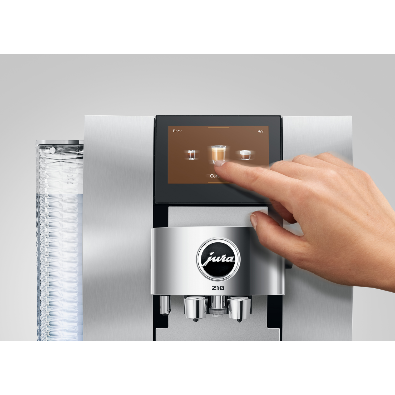 A hand touches a coffee machine screen. The screen shows coffee options. Jura logo is visible. Machine is silver and black.