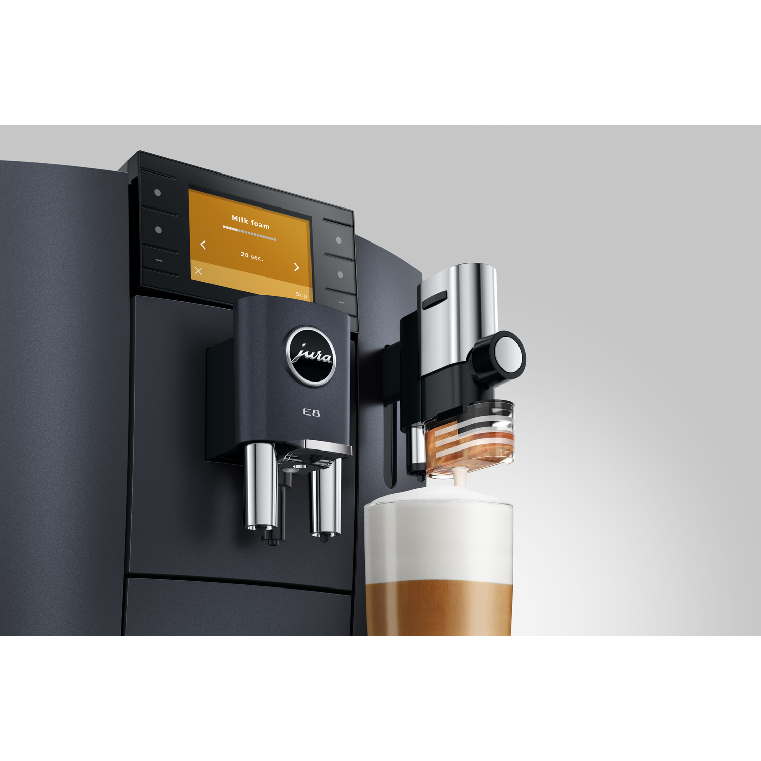 A coffee machine is making milk foam. The machine is black. A cup with coffee and milk is on the right.