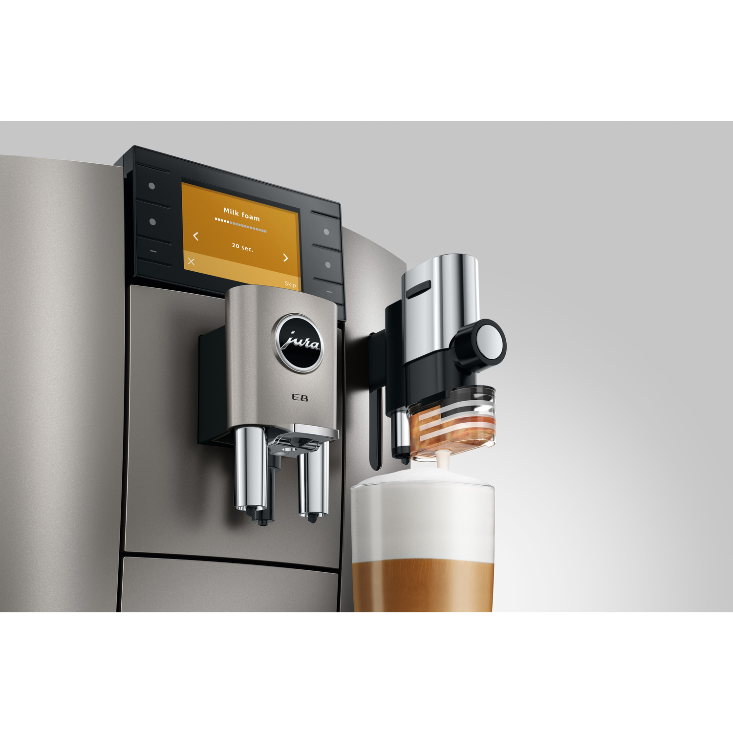 A Jura E8 coffee machine is dispensing milk foam into a glass. The machine has a digital display showing "Milk foam".
