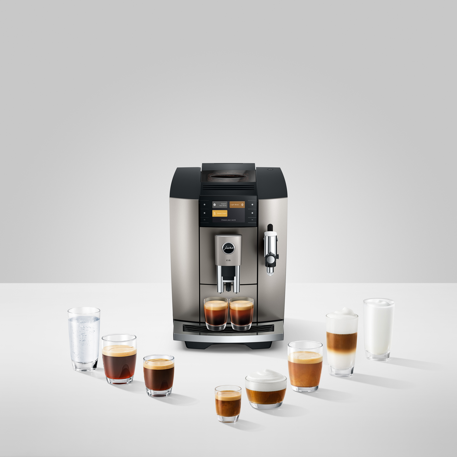 A silver espresso machine with various coffee drinks in glasses around it. Drinks include espresso, latte, and water.