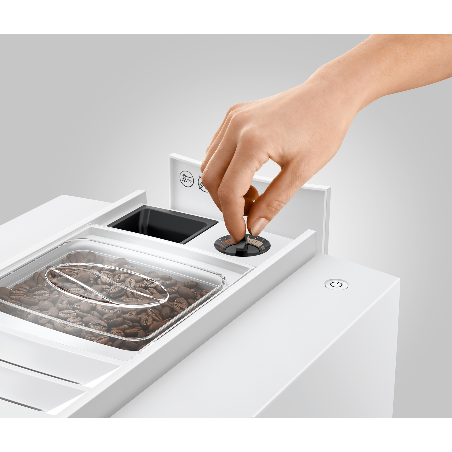 A hand adjusts a coffee machine's grinder setting. Visible are coffee beans in a clear container, a power button, and a black grinder setting.