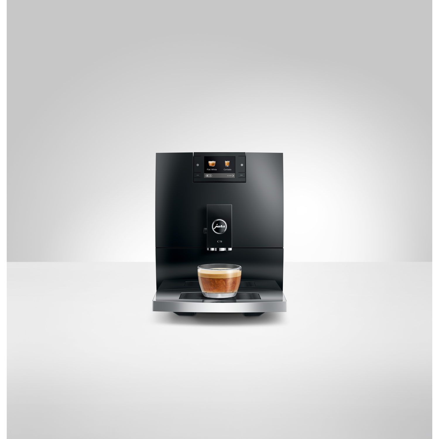 A black Jura C9 coffee machine with a cup of espresso on the tray. A screen shows drink options. White background.