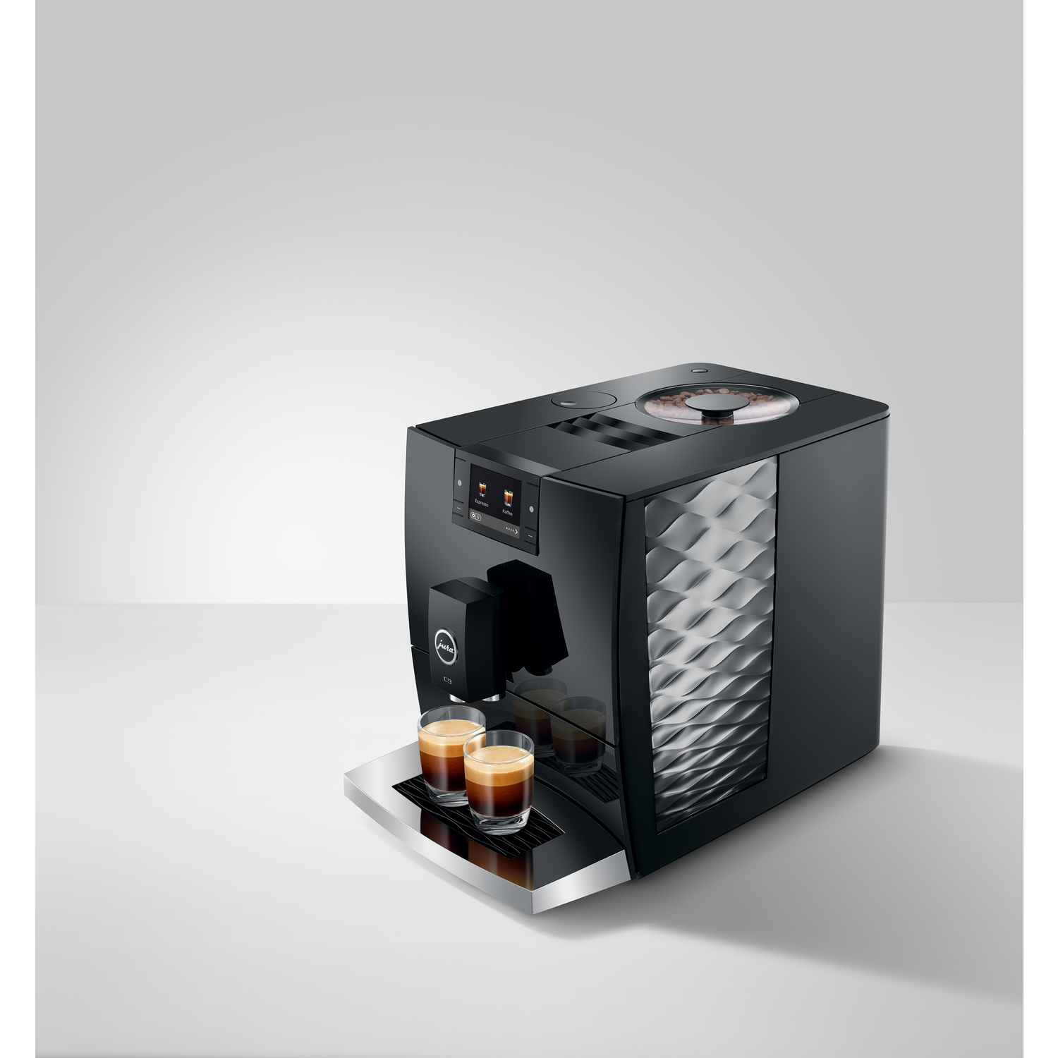 Black espresso machine with two glasses of espresso on a white surface. The machine has a bean container on top.