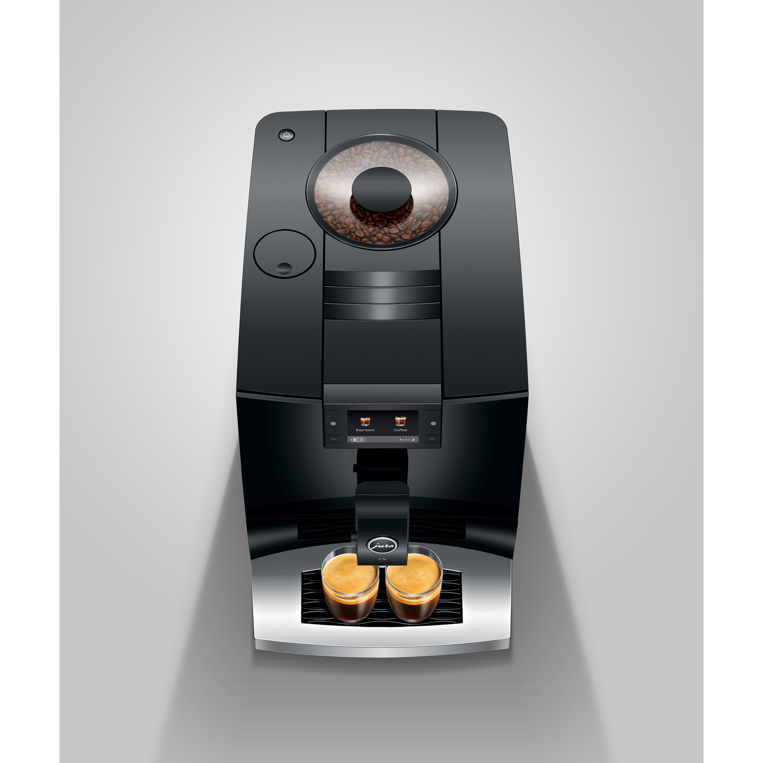 Black Jura coffee machine with coffee beans in a transparent container. Two glasses of espresso are below. The background is white.