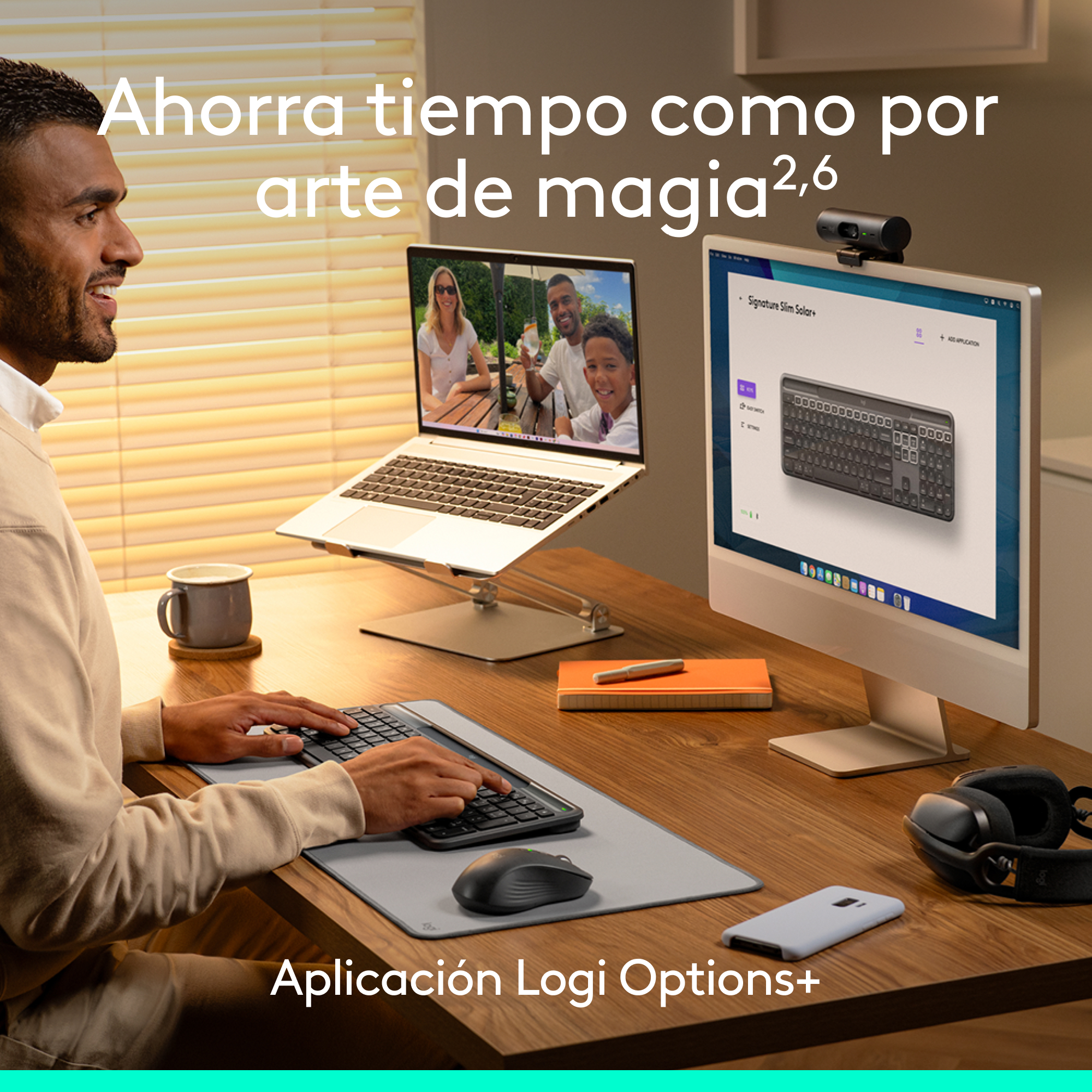 Un hombre sonríe mientras usa una computadora. Una computadora portátil y un monitor muestran un teclado. Un ratón y un teclado están sobre el escritorio.