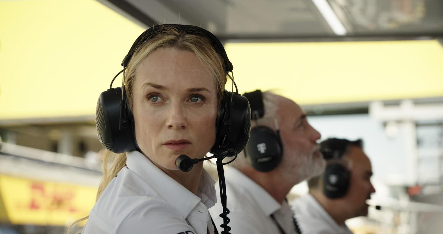 Eine Frau mit blonden Haaren und Headset, in einem weißen Hemd, schaut aufmerksam. Im Hintergrund sind zwei Männer zu sehen.