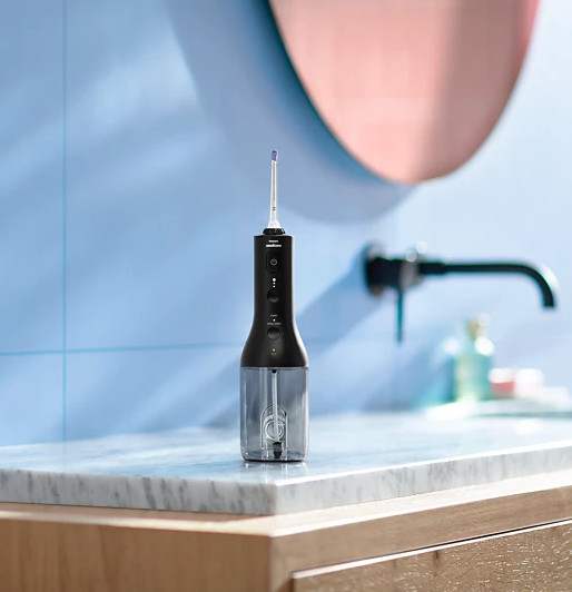 Czarny irygator do jamy ustnej na marmurowym blacie w łazience. Różowe lustro i czarna bateria w tle.