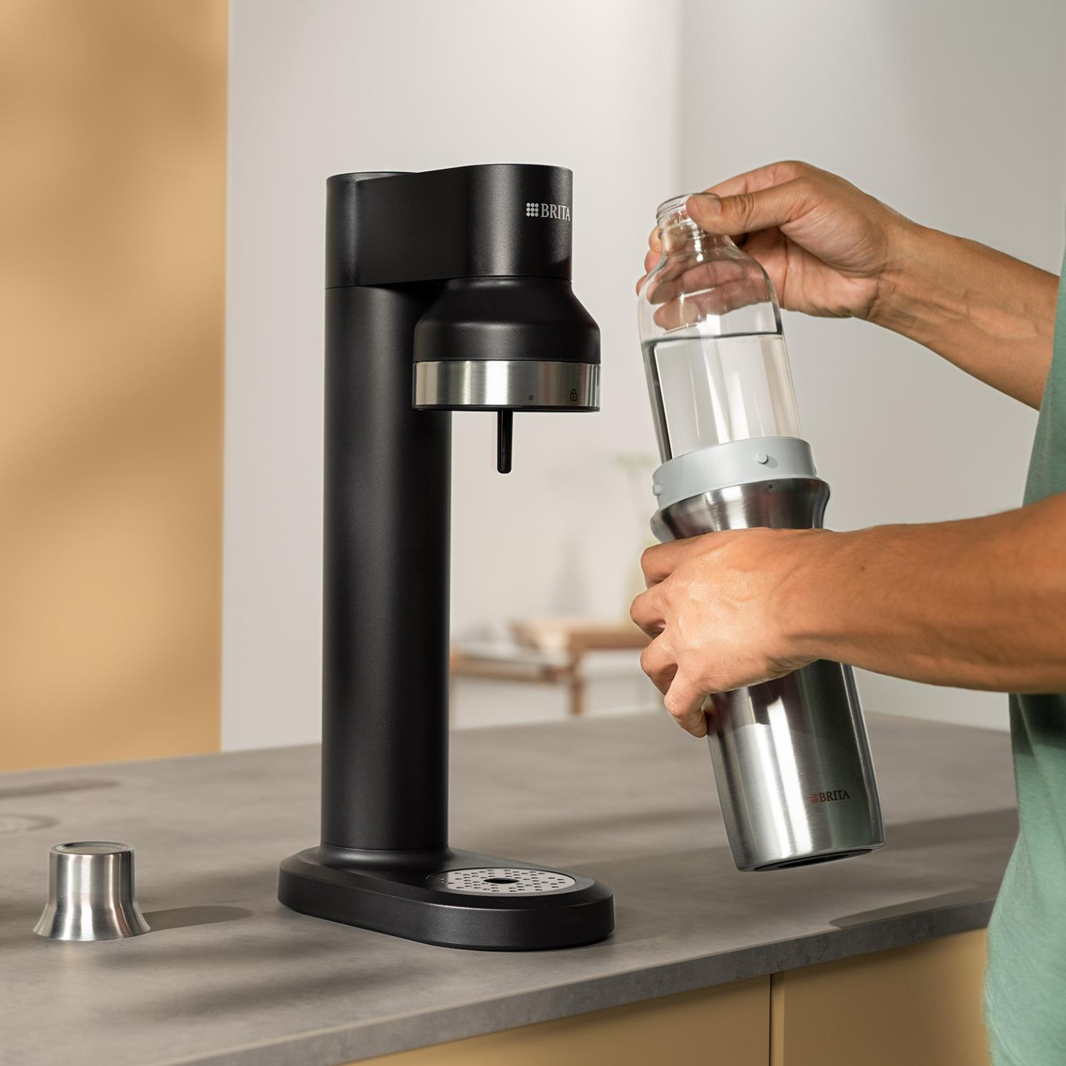 Osoba napełnia butelkę wodą z czarnego dozownika wody. Butelka i dozownik mają logo marki Brita.