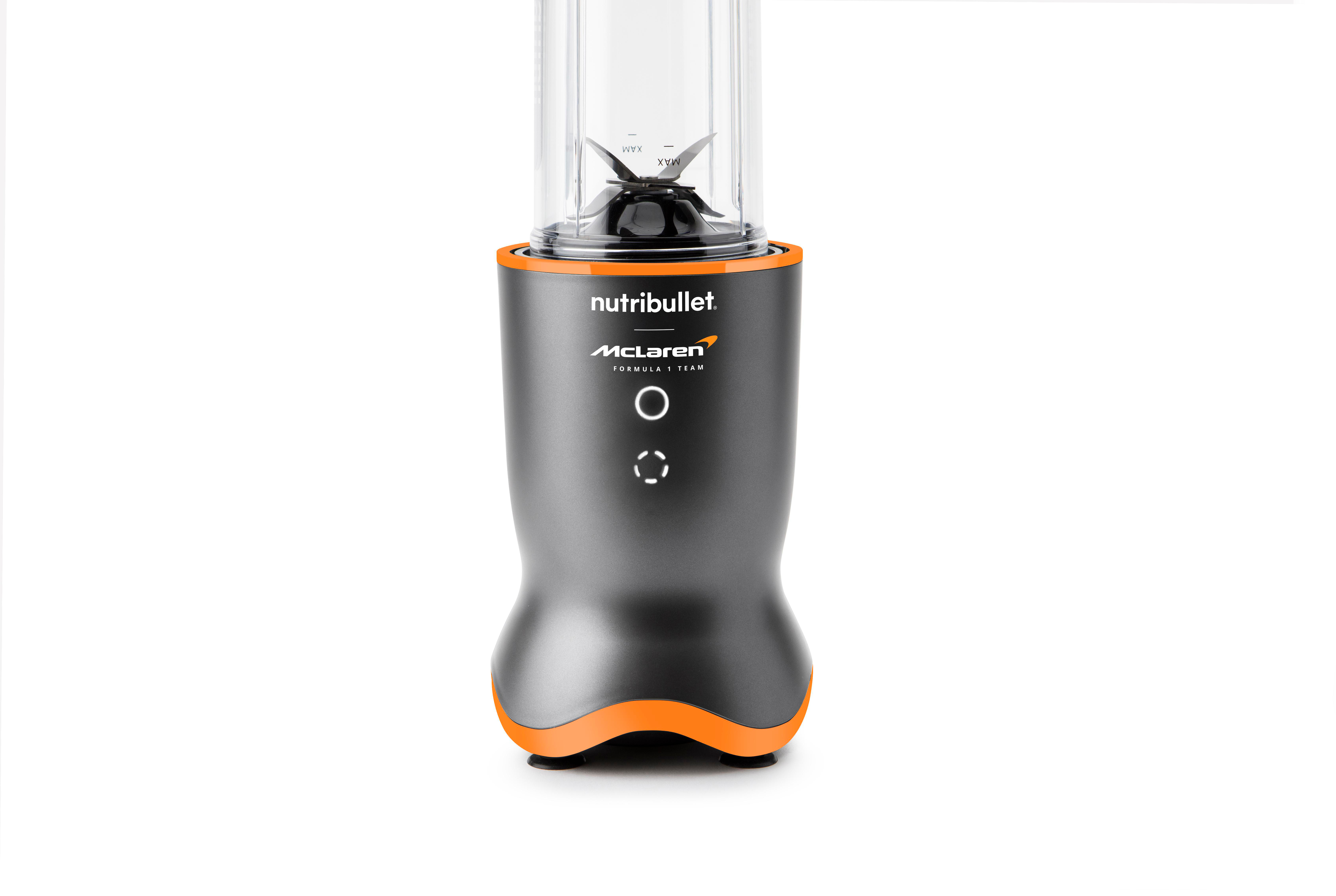 Ein Nutribullet-Mixer mit transparentem Behälter und schwarzen Klingen, grauem Gehäuse und orangefarbenen Akzenten. McLaren-Logo sichtbar.