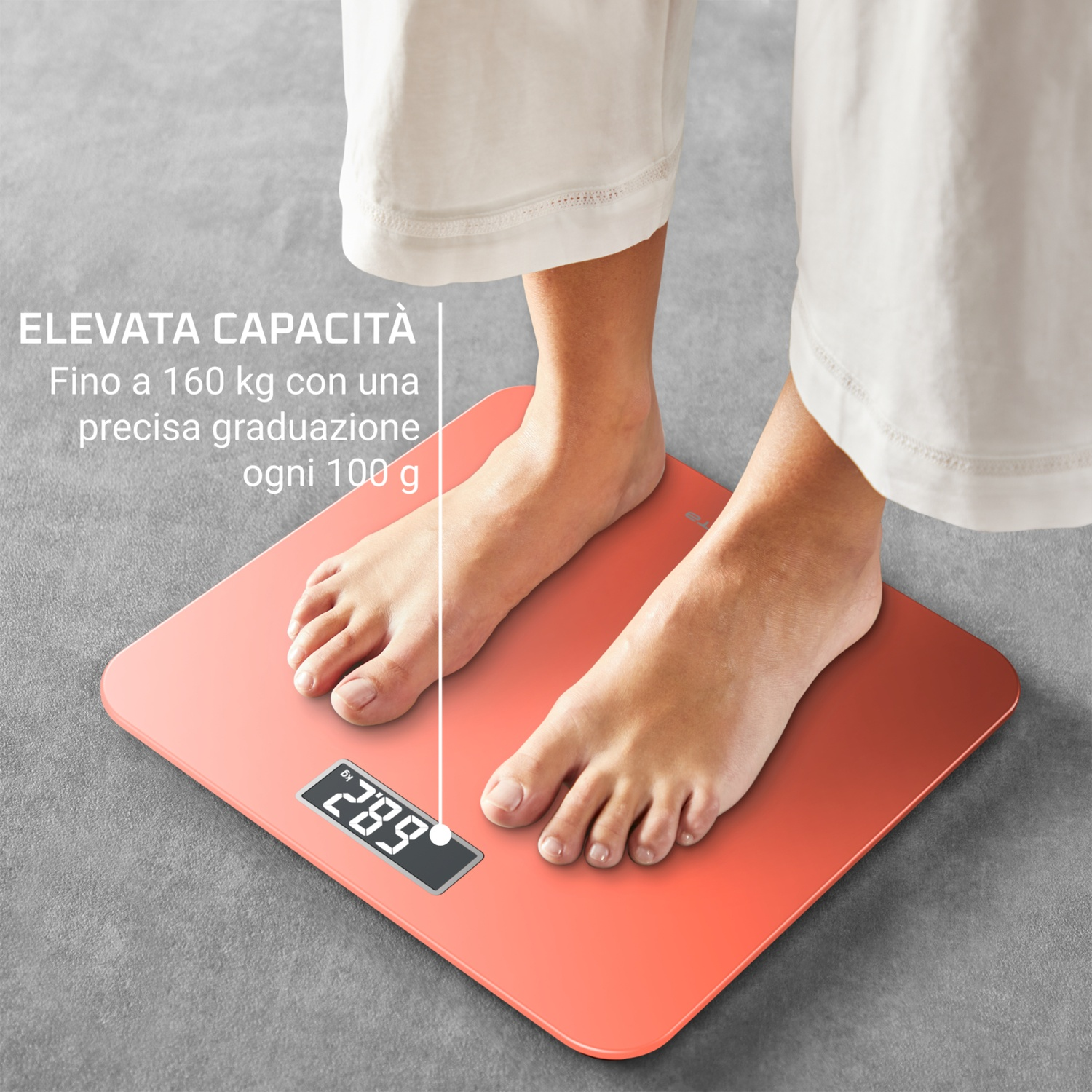 Piedi su una bilancia corallo che mostra 28,9. La bilancia è su un pavimento grigio, con pantaloni bianchi visibili.
