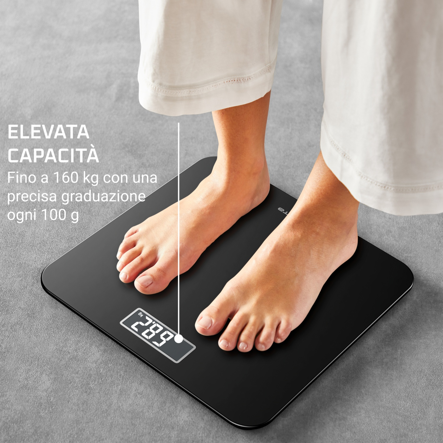 Una persona è in piedi su una bilancia nera. La bilancia mostra 28,9 kg. La persona indossa pantaloni bianchi. Testo: 'Capacità elevata, fino a 160 kg'.
