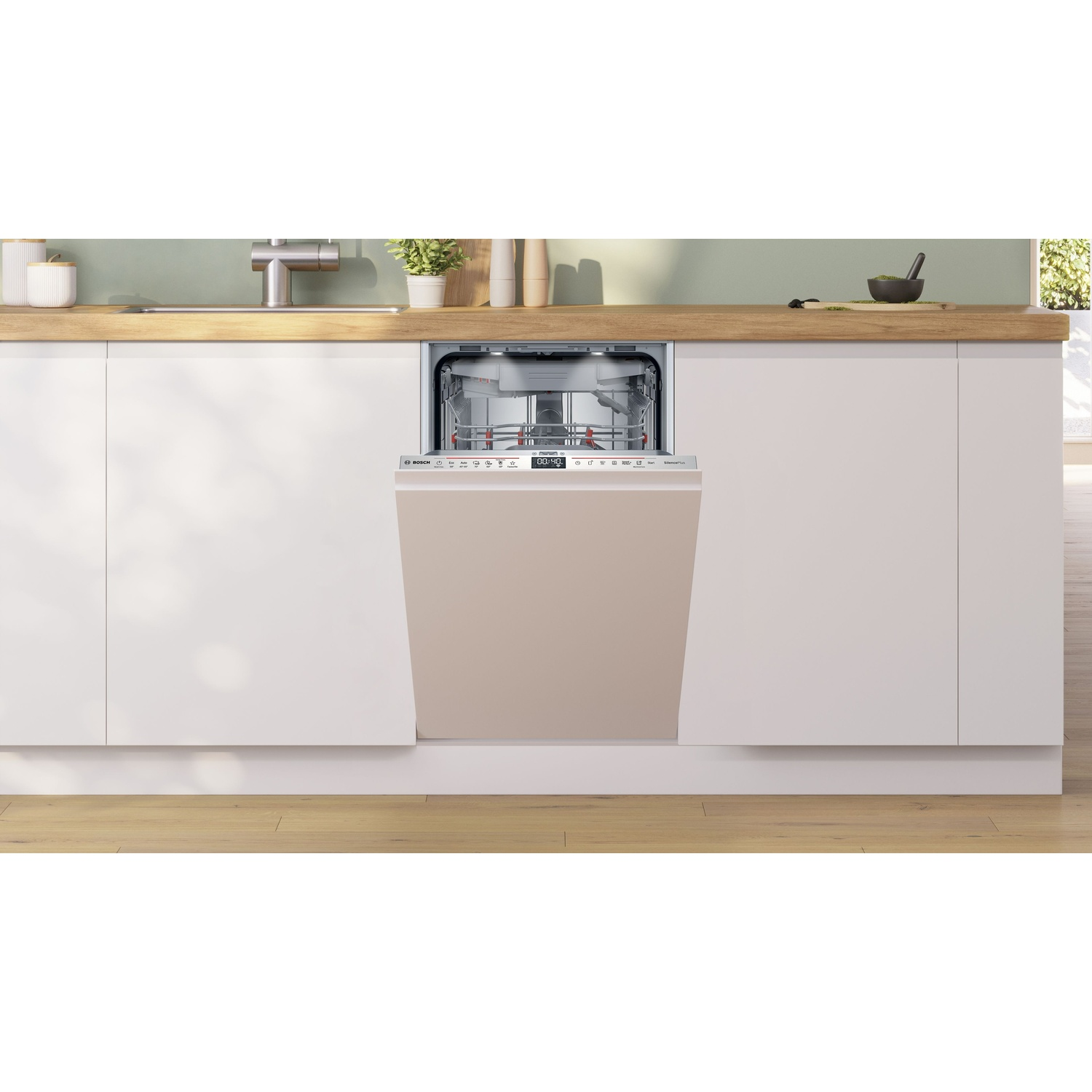 Una lavastoviglie a incasso con porta beige è aperta. È in una cucina bianca con piano di lavoro in legno. Piante sullo sfondo.