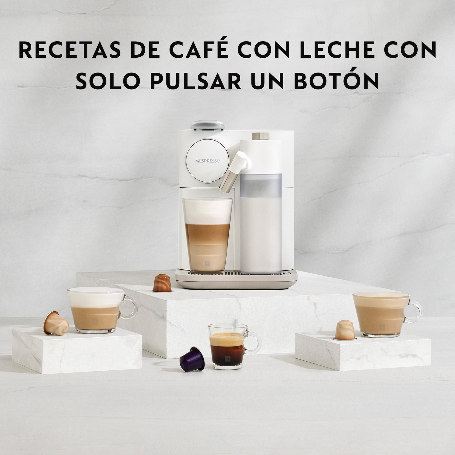 Una máquina Nespresso blanca se muestra con tazas de café y leche. Cápsulas de café y bebidas están sobre pedestales blancos.
