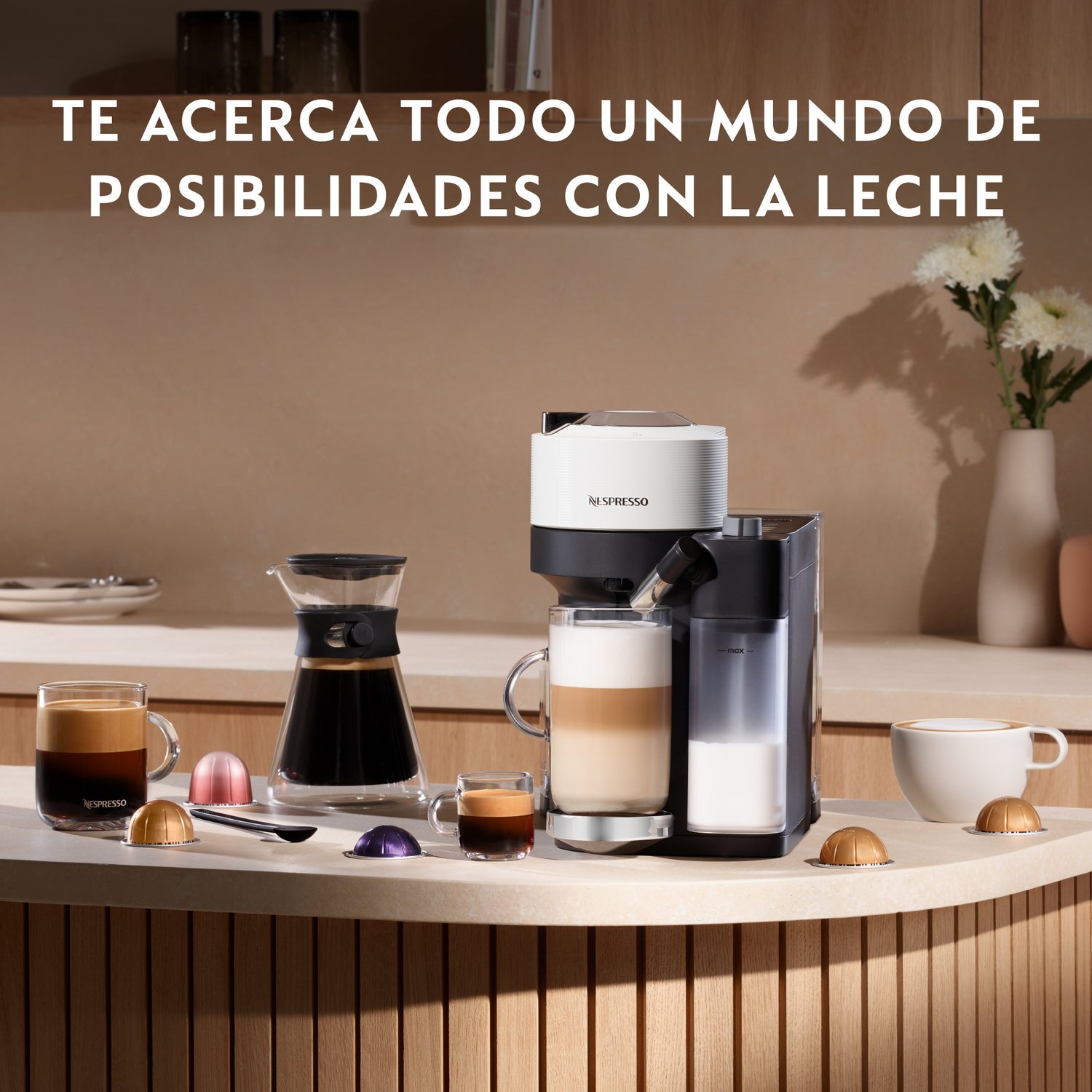 Cafetera con latte, espresso y capuchino sobre una encimera. También hay cápsulas de café, una jarra de vidrio y flores.