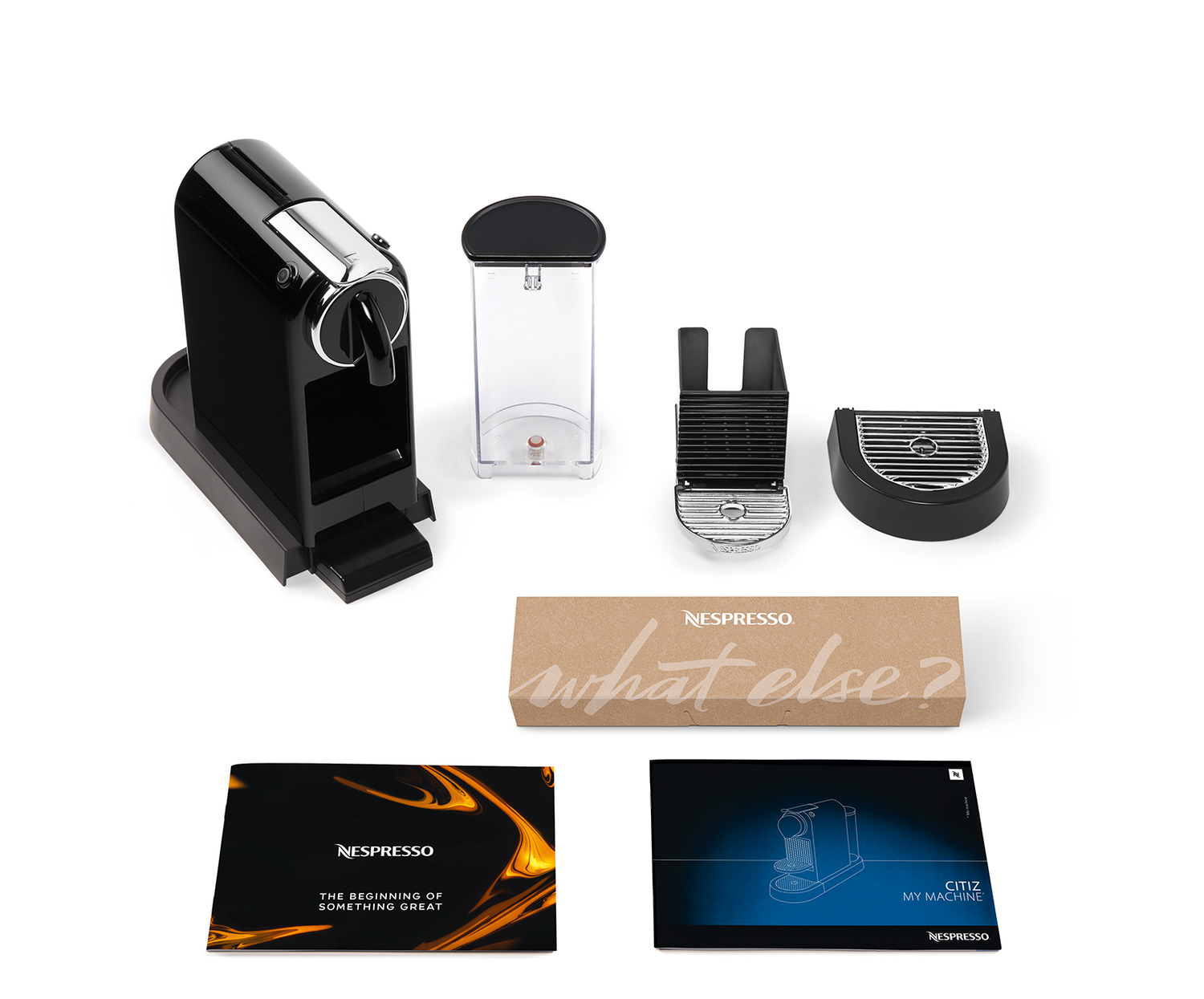 Una cafetera Nespresso negra desmontada con componentes: depósito de agua, contenedor de cápsulas usadas, bandeja de goteo y manuales.