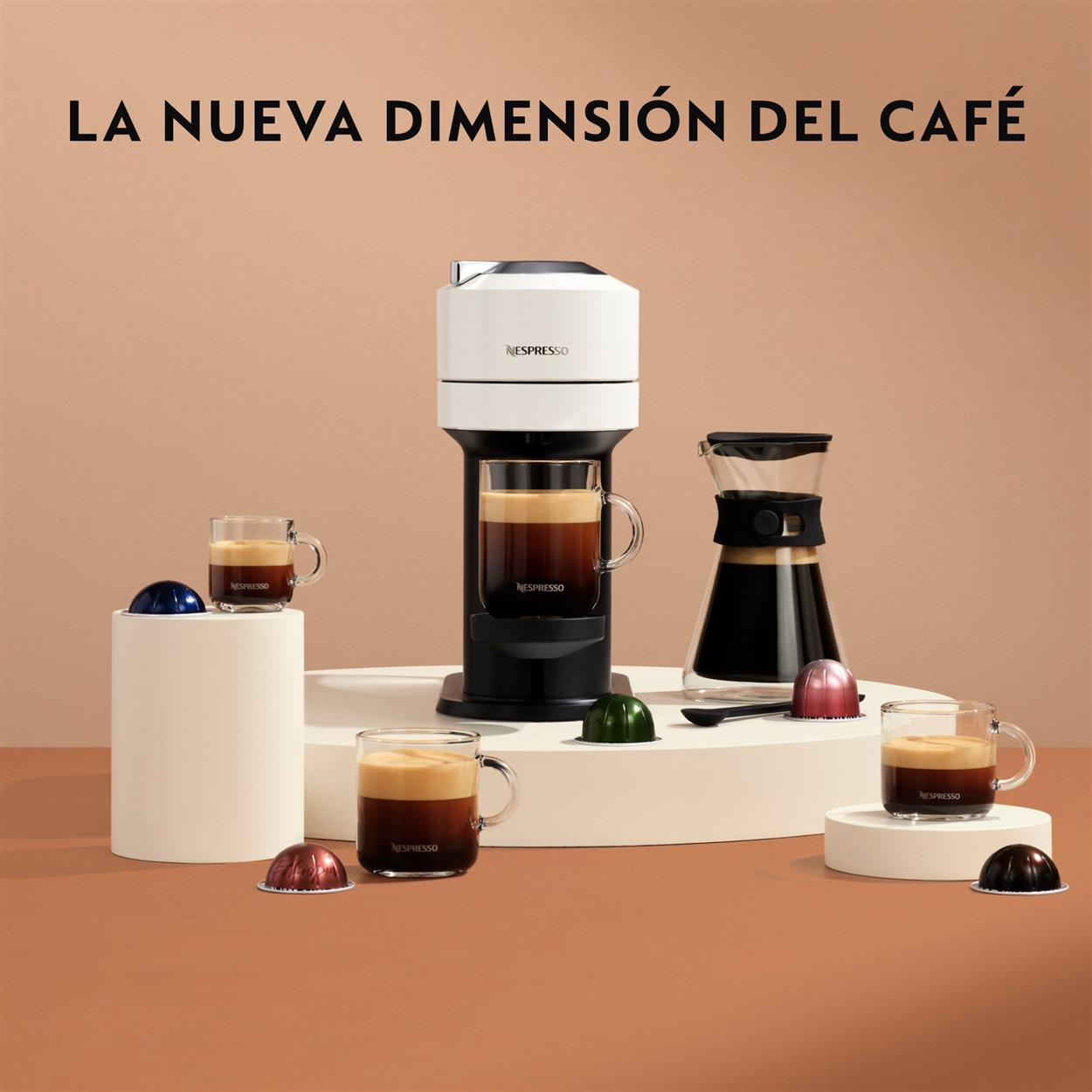 Una cafetera con tazas y cápsulas de café, una cafetera de cristal. Texto 'LA NUEVA DIMENSIÓN DEL CAFÉ' arriba.