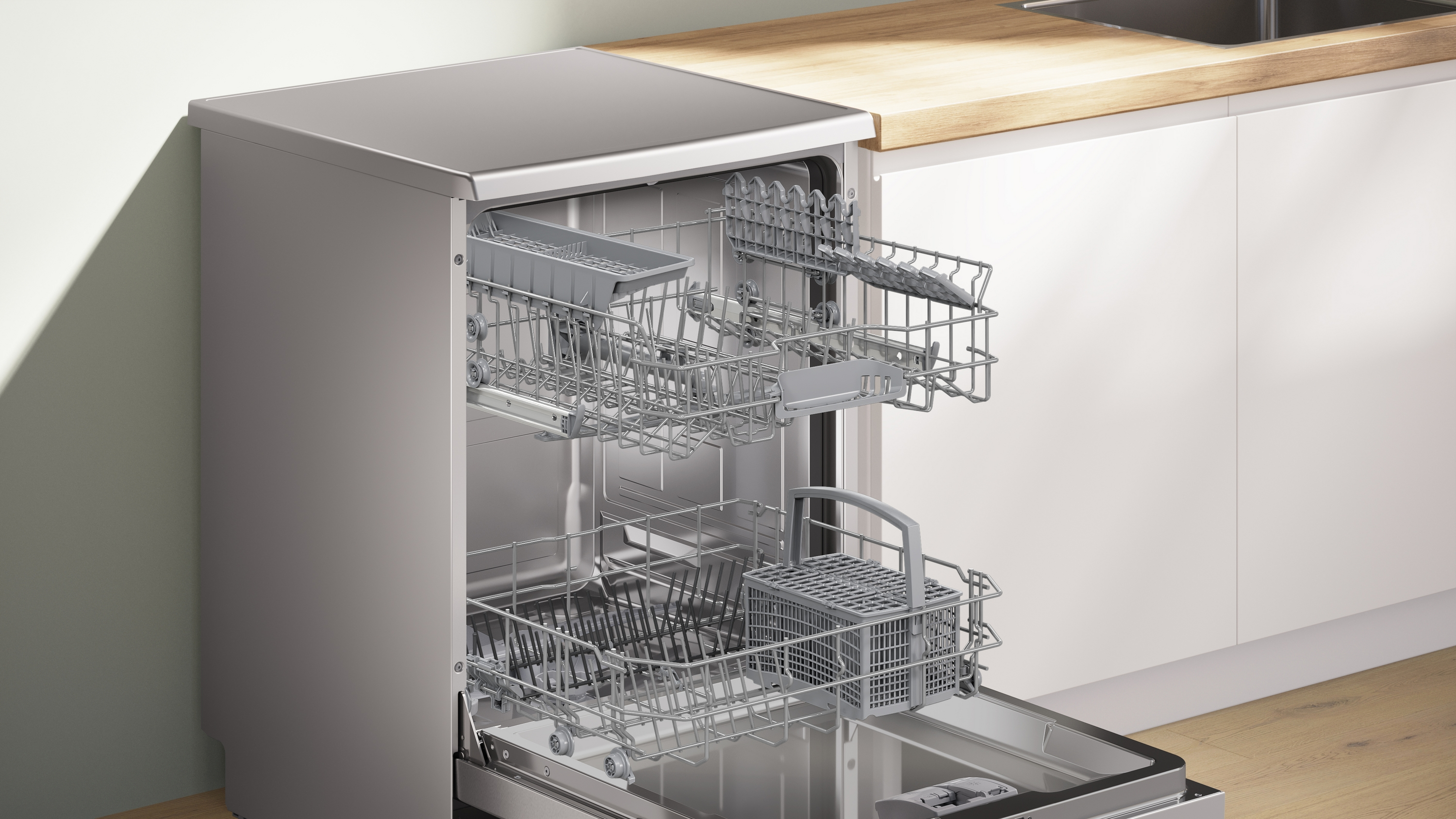 Een open vaatwasser met lege rekken. De machine is zilverkleurig, geplaatst tegen een wit en houten keukeninterieur.