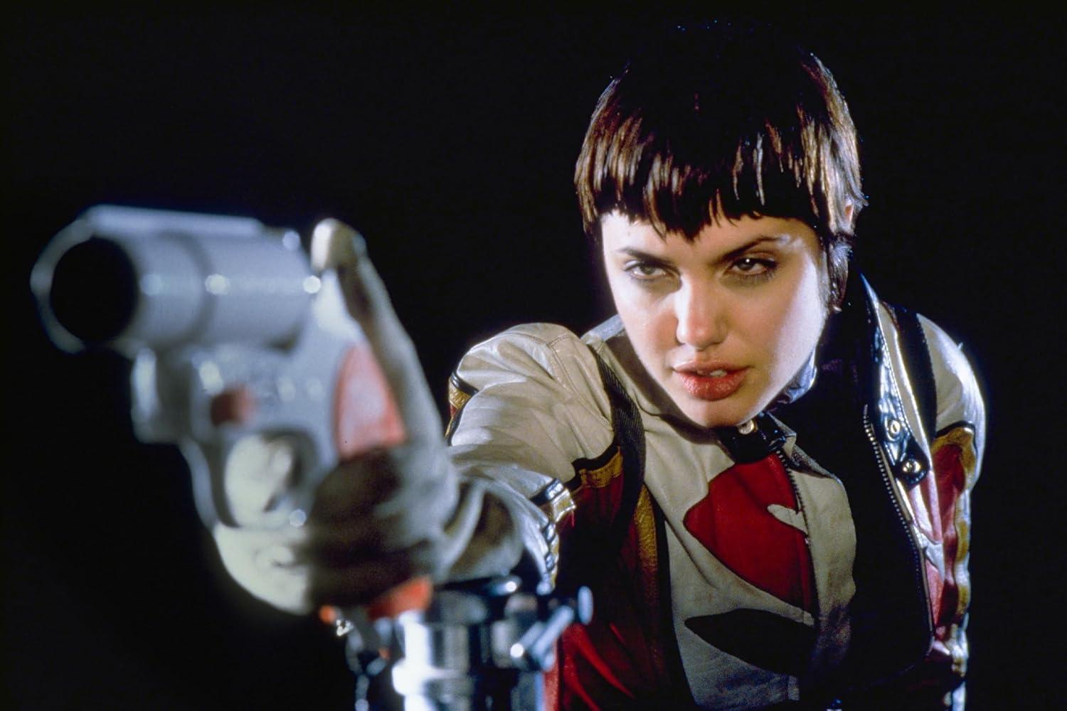 Eine Frau mit kurzen Haaren zielt mit einer futuristischen Waffe. Sie trägt eine weiß-rot-schwarze Jacke und starrt intensiv in die Kamera.