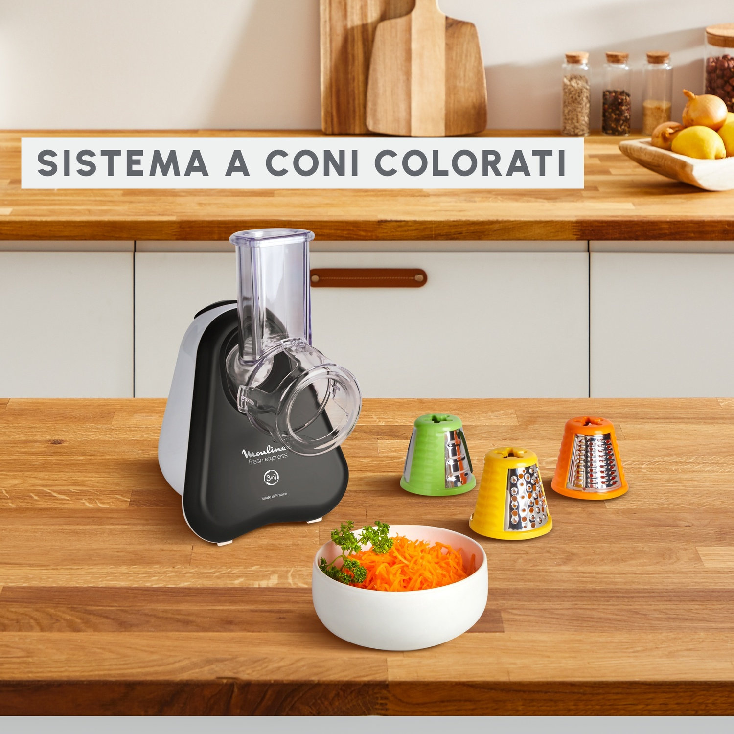 Un robot da cucina con coni colorati è su un piano di lavoro in legno. Ci sono ciotole con carote grattugiate e spezie sullo sfondo.