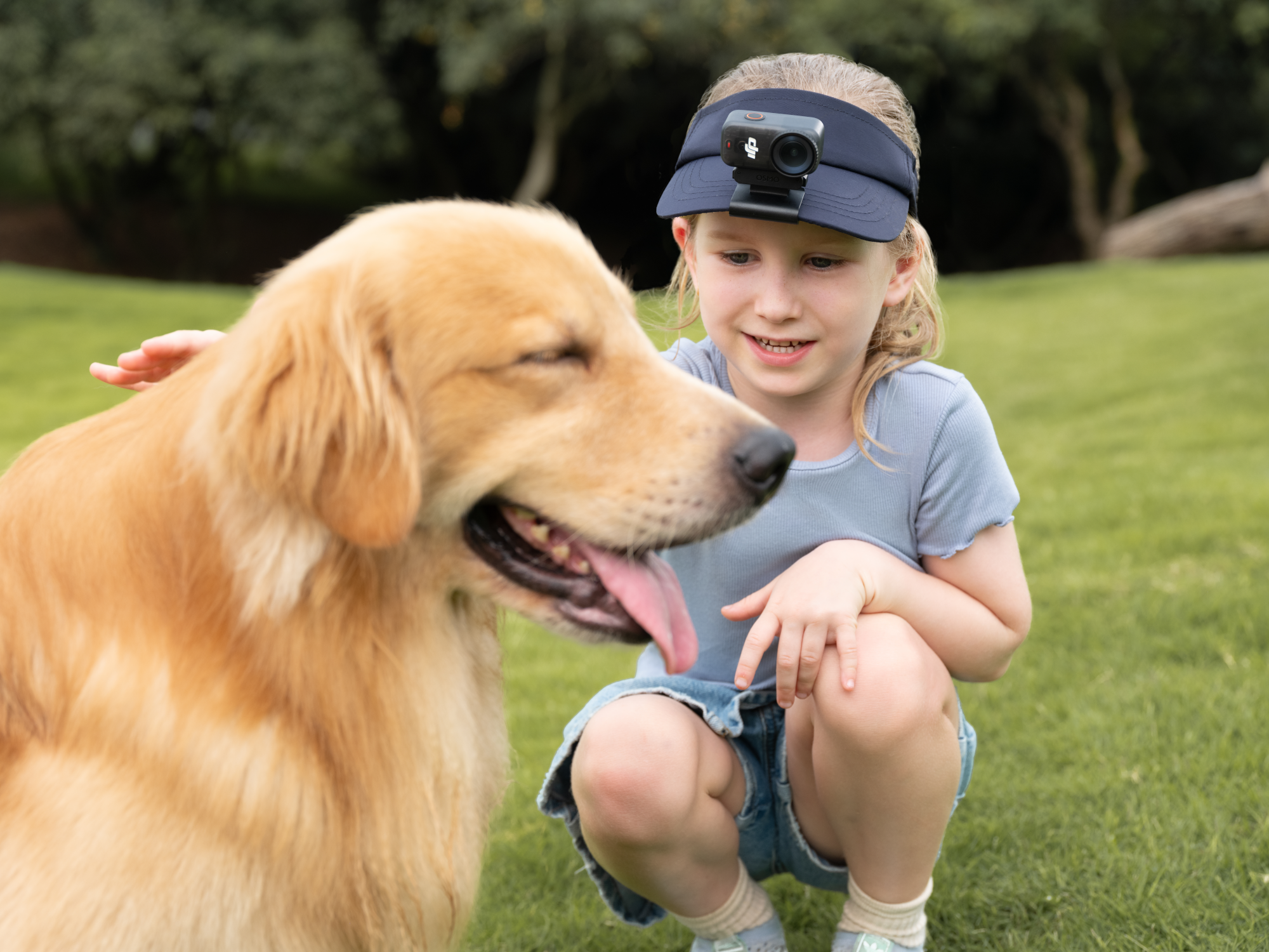 Une fille en visière caresse un golden retriever. Le chien tire la langue. Ils sont sur l'herbe verte.