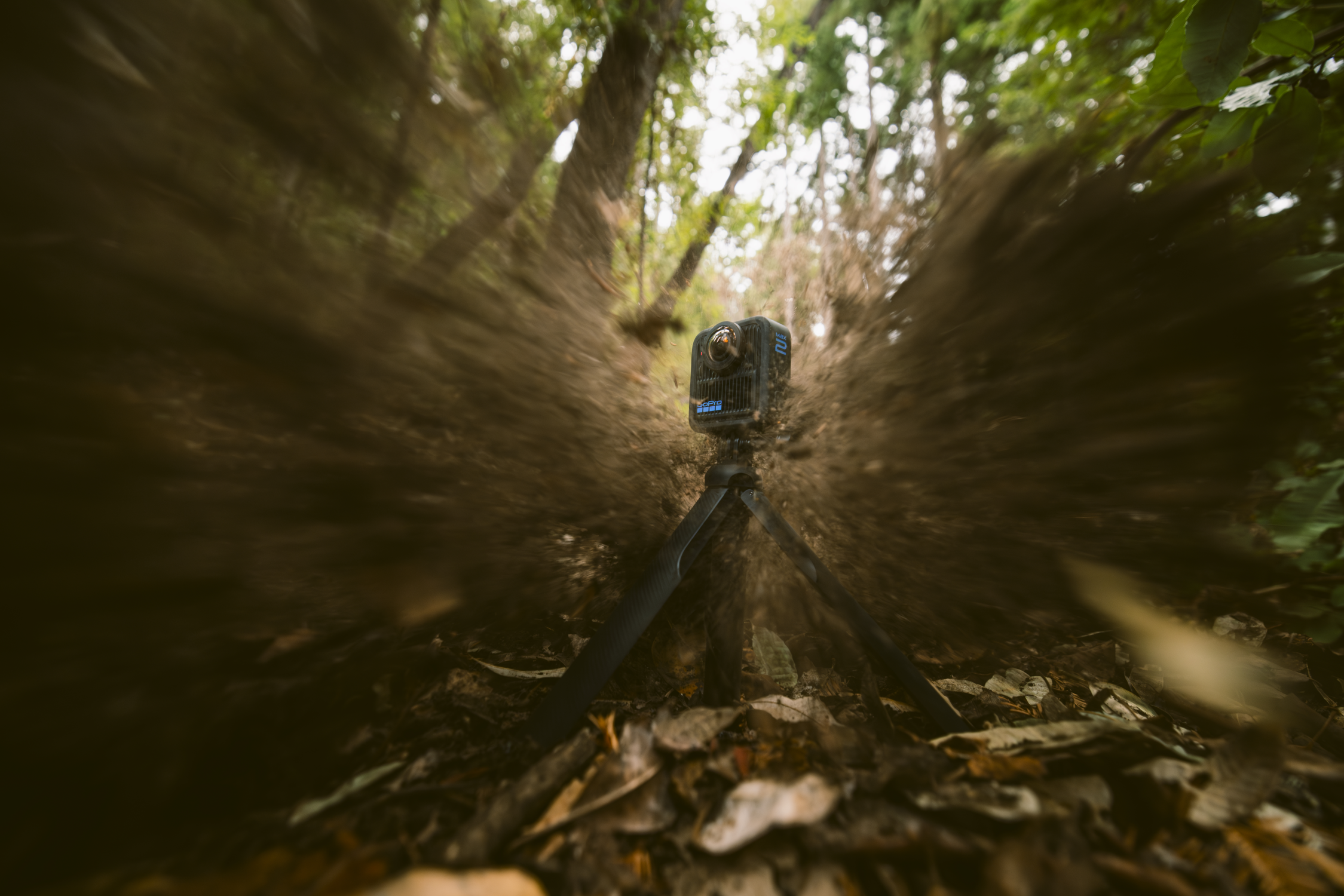 Eine GoPro-Kamera auf einem Stativ steht auf einem Waldweg. Die Aufnahme verschwimmt und erzeugt einen tunnelförmigen Effekt zur Kamera hin.