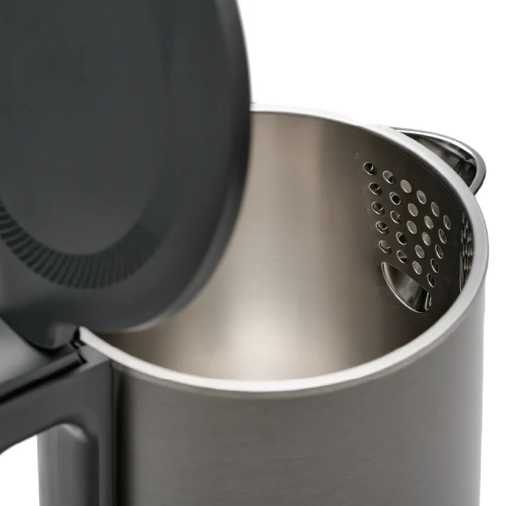 Gros plan sur une bouilloire en acier inoxydable. Le couvercle est partiellement ouvert, révélant l'intérieur. Métal perforé sur le côté.