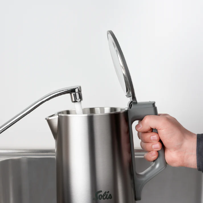 Une bouilloire est remplie d'eau d'un robinet. Une main tient la poignée de la bouilloire. La bouilloire est en acier inoxydable.